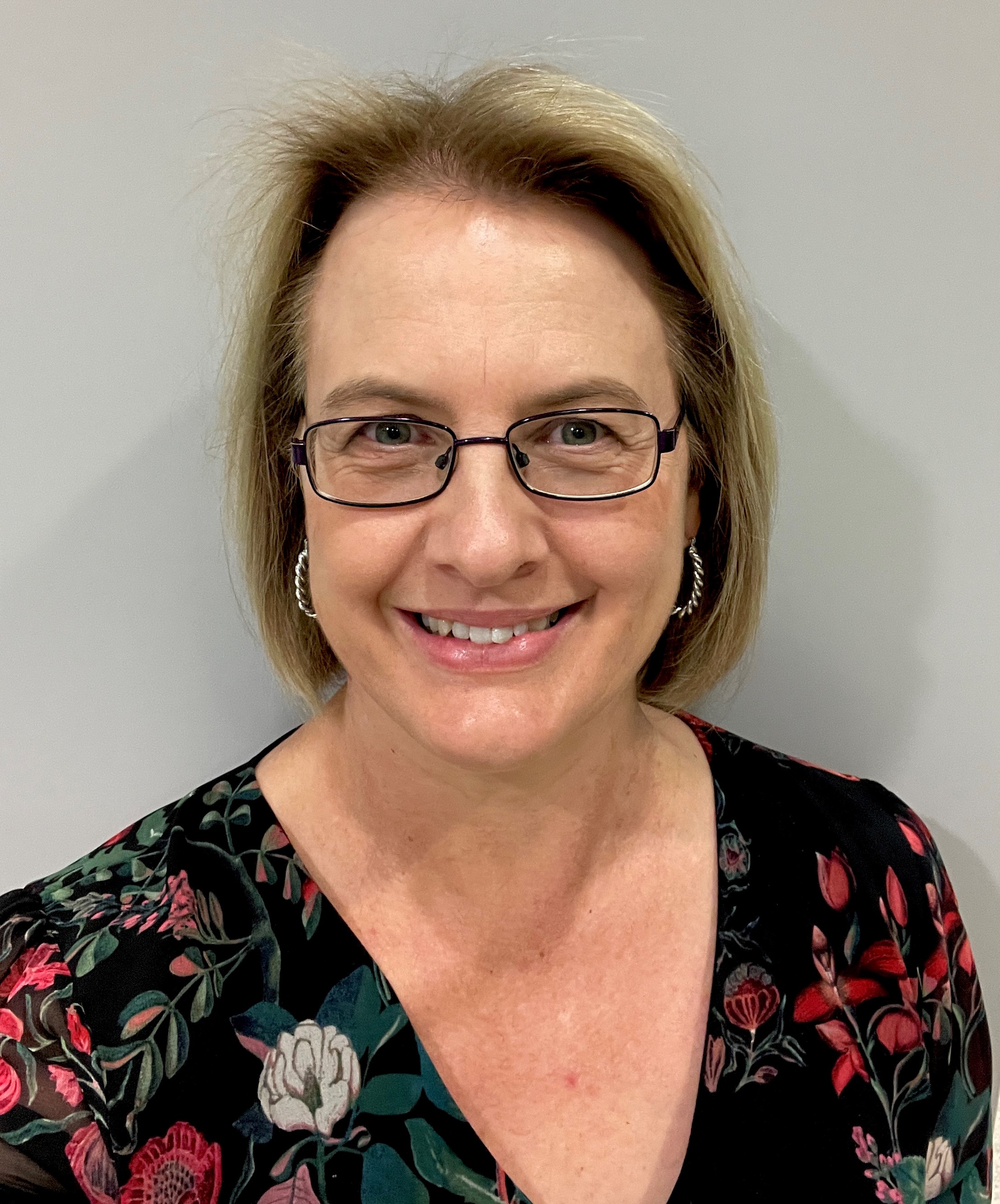 Profile photo of a woman wearing glasses in front of a grey background. 