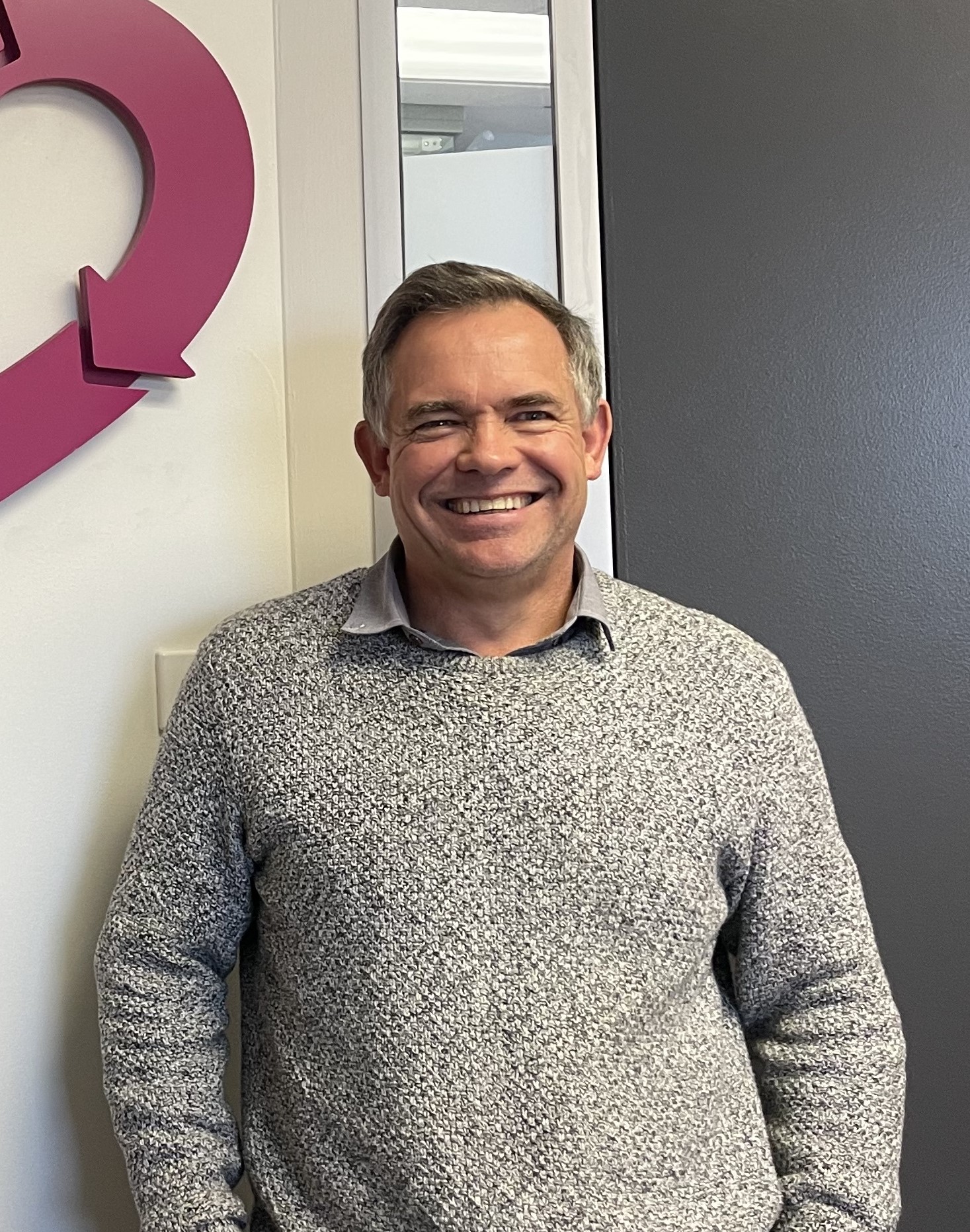 Man in a grey sweater smiling at the camera