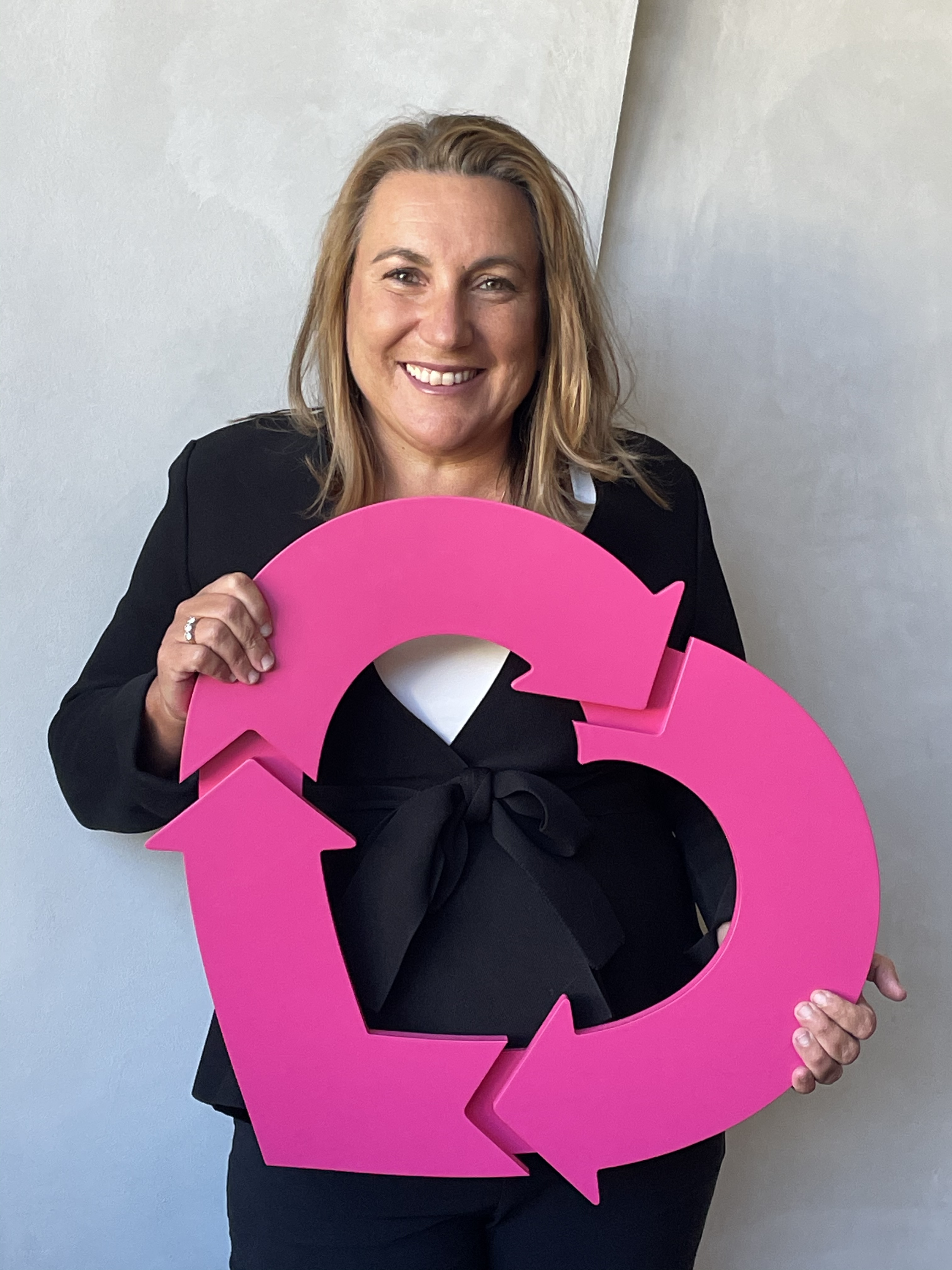 Woman in a black suit, holding a large DonateLife heart, smiling at the camera.