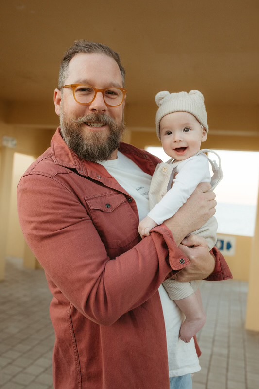 Man in a muted orange blazer is holding a happy baby