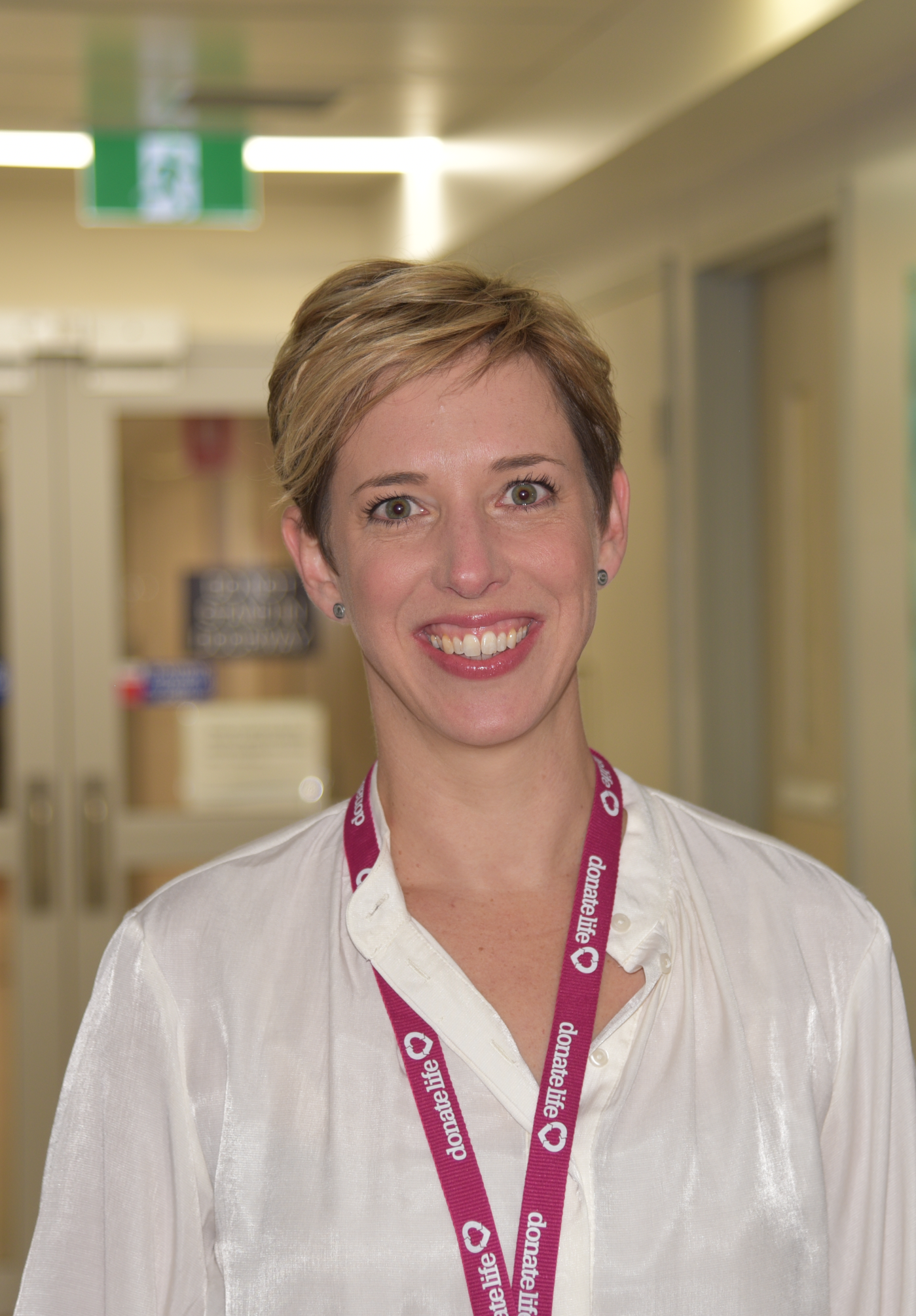 Woman with a blonde pixie cut, wearing a white button up shirt, smiling at the camera. 