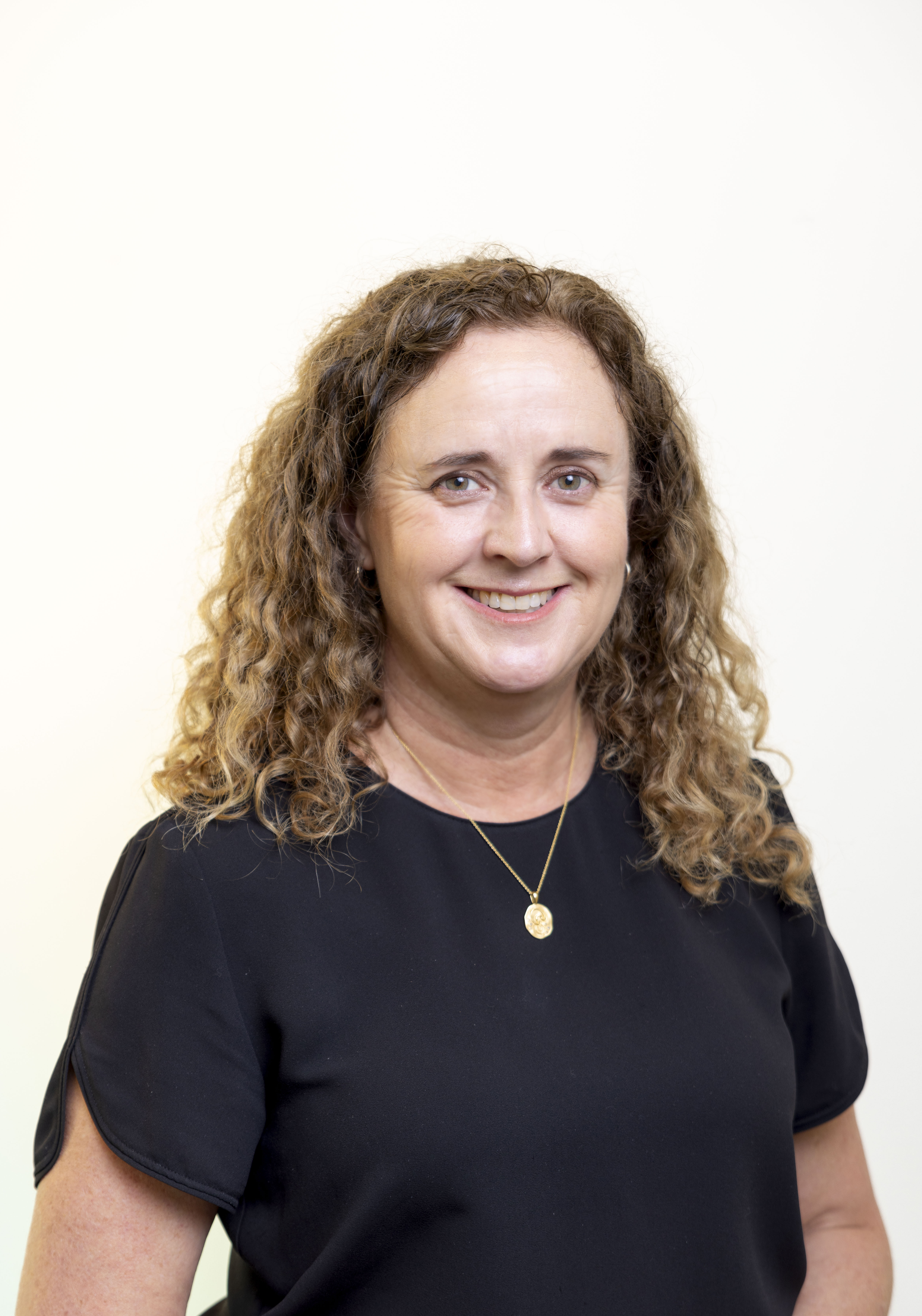 Woman with shoulder length curly hair, wearing a black shirt, smiling at the camera