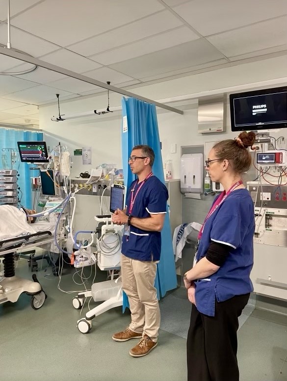 Two hospital staff in scrubs deliver a presentation in a hospital ICU