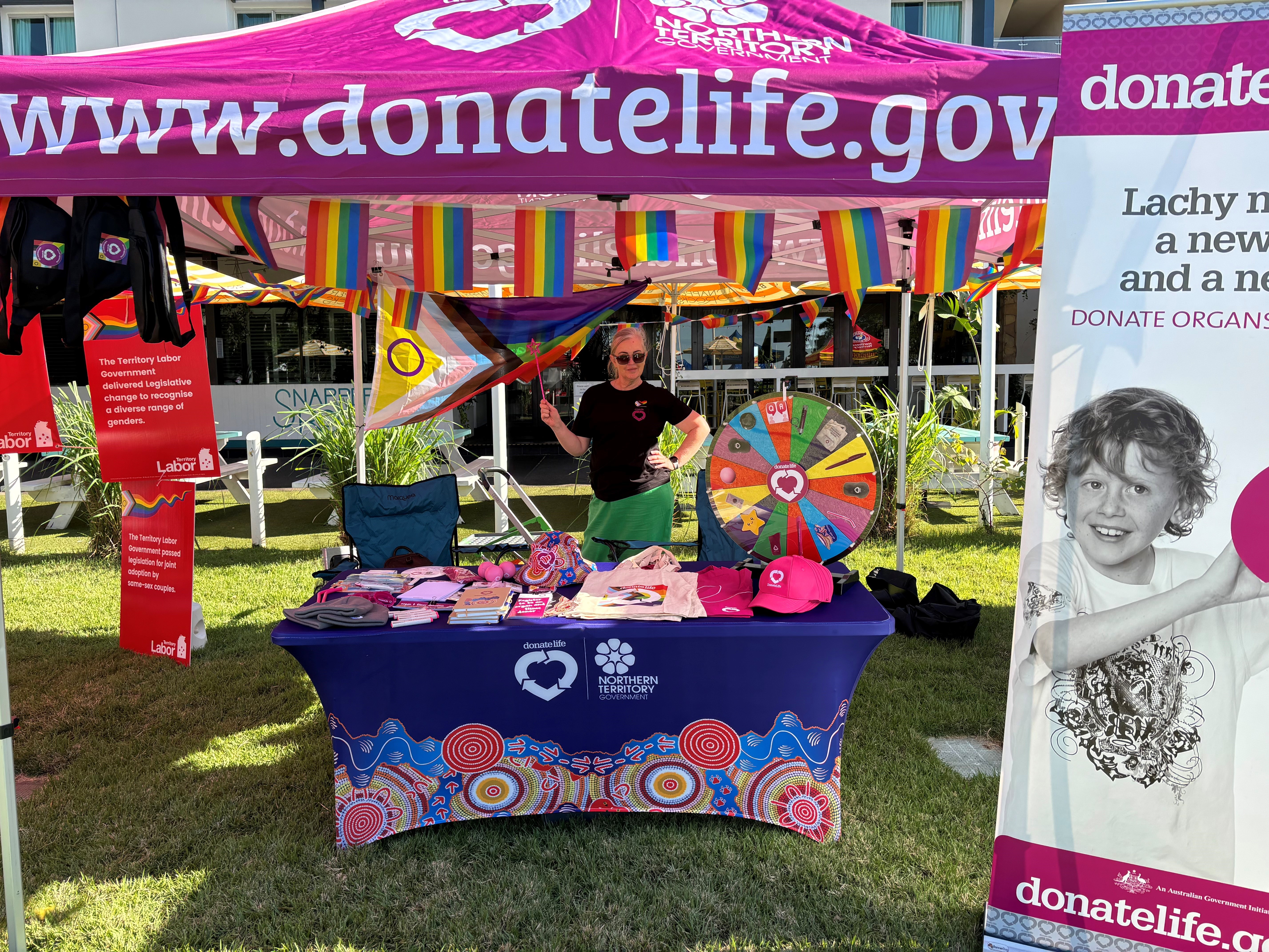 A woman poses behind a colourful DonateLife stand at a Pride event.