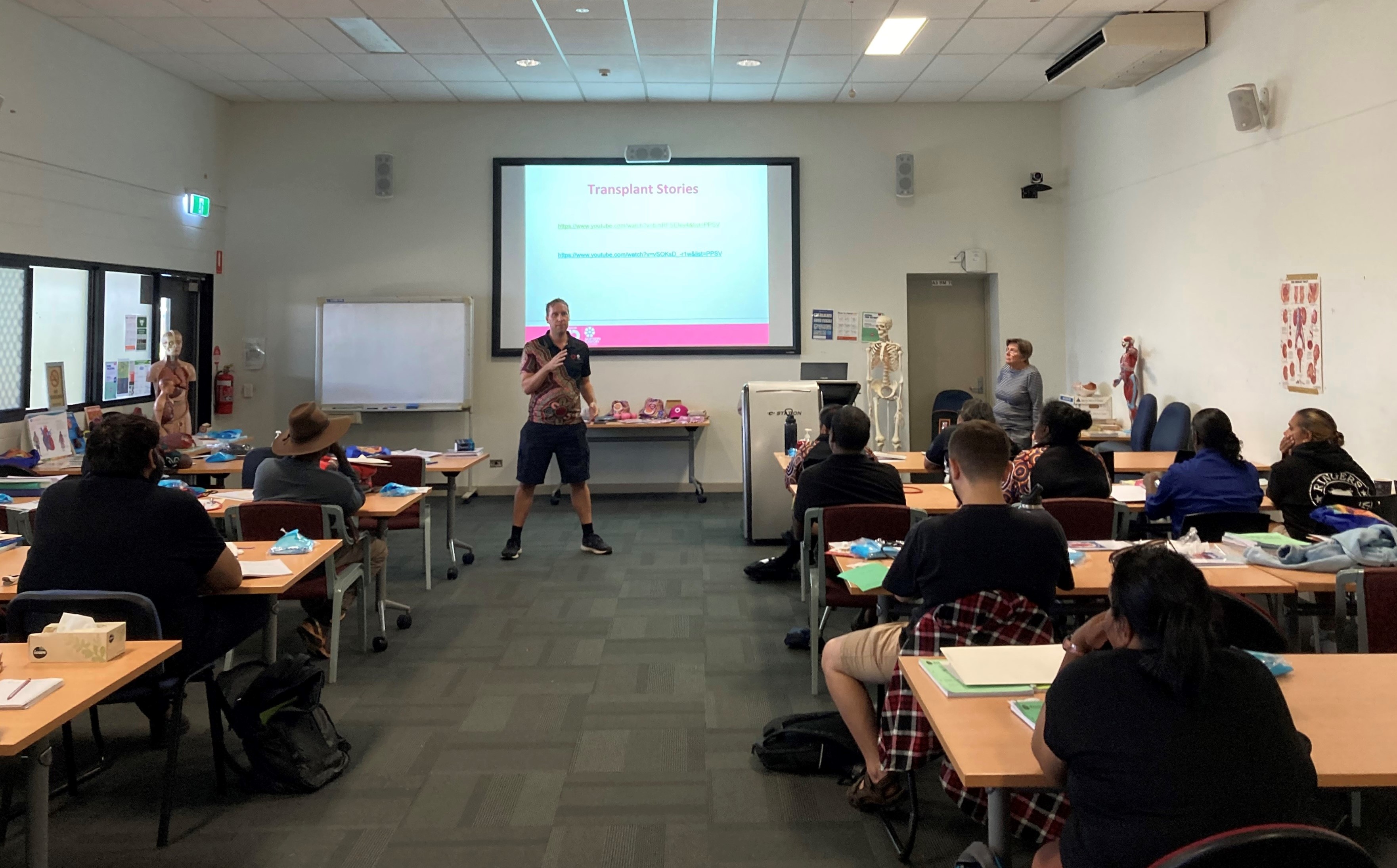 A man delivers a presentation to a classroom full of students.