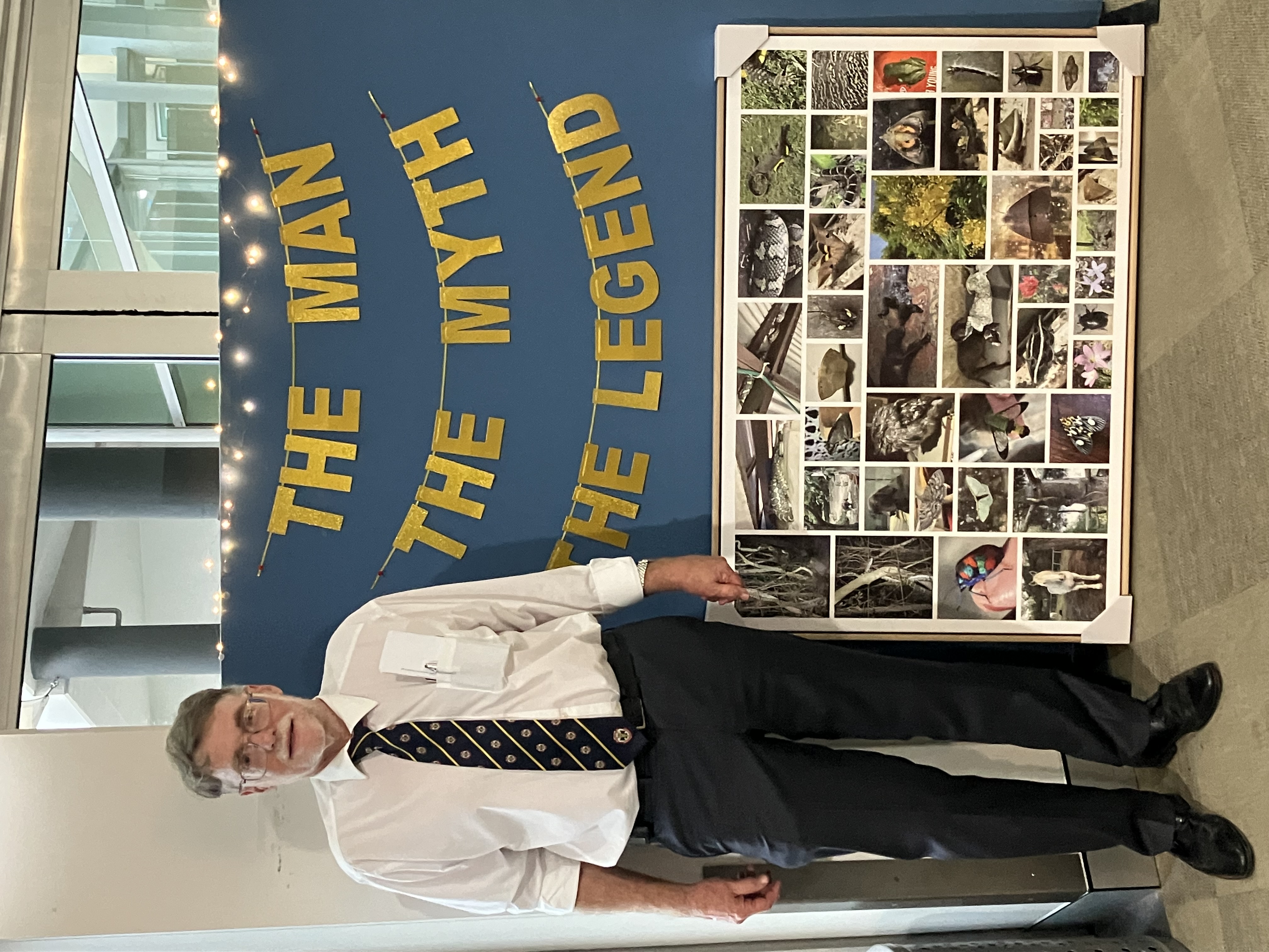 A photo of a man standing next to a wall with a letter banner that says ‘The Man, the Myth, the Legend’. Under the banner is a large, framed photo collage