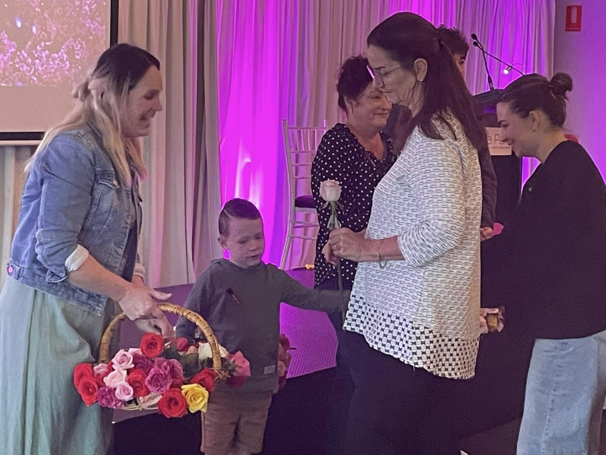 A young woman hands out roses from a basket to attendees at a Service of Remembrance event. 