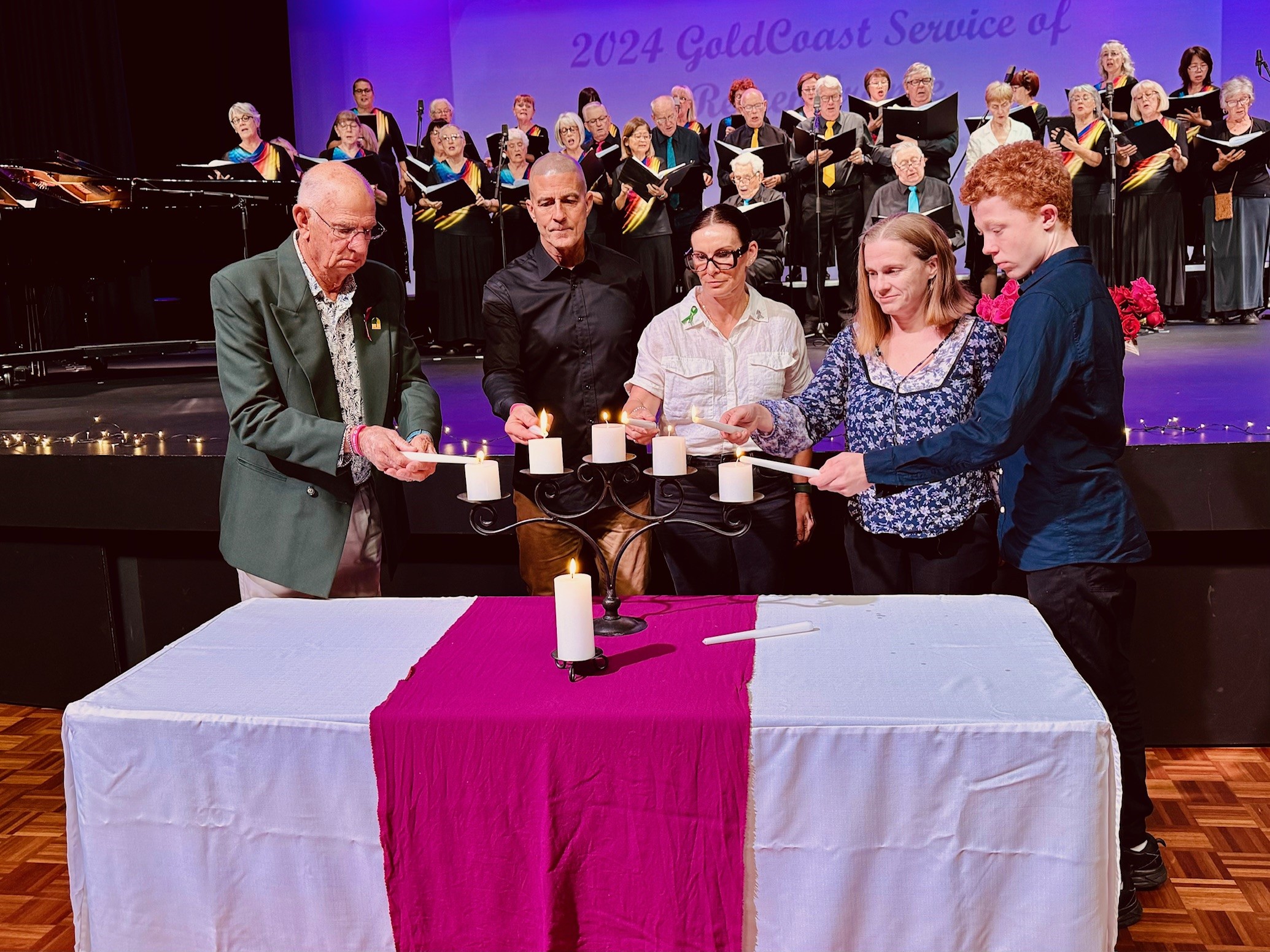 Five people light candles in front of a choir at a Service of Remembrance event.