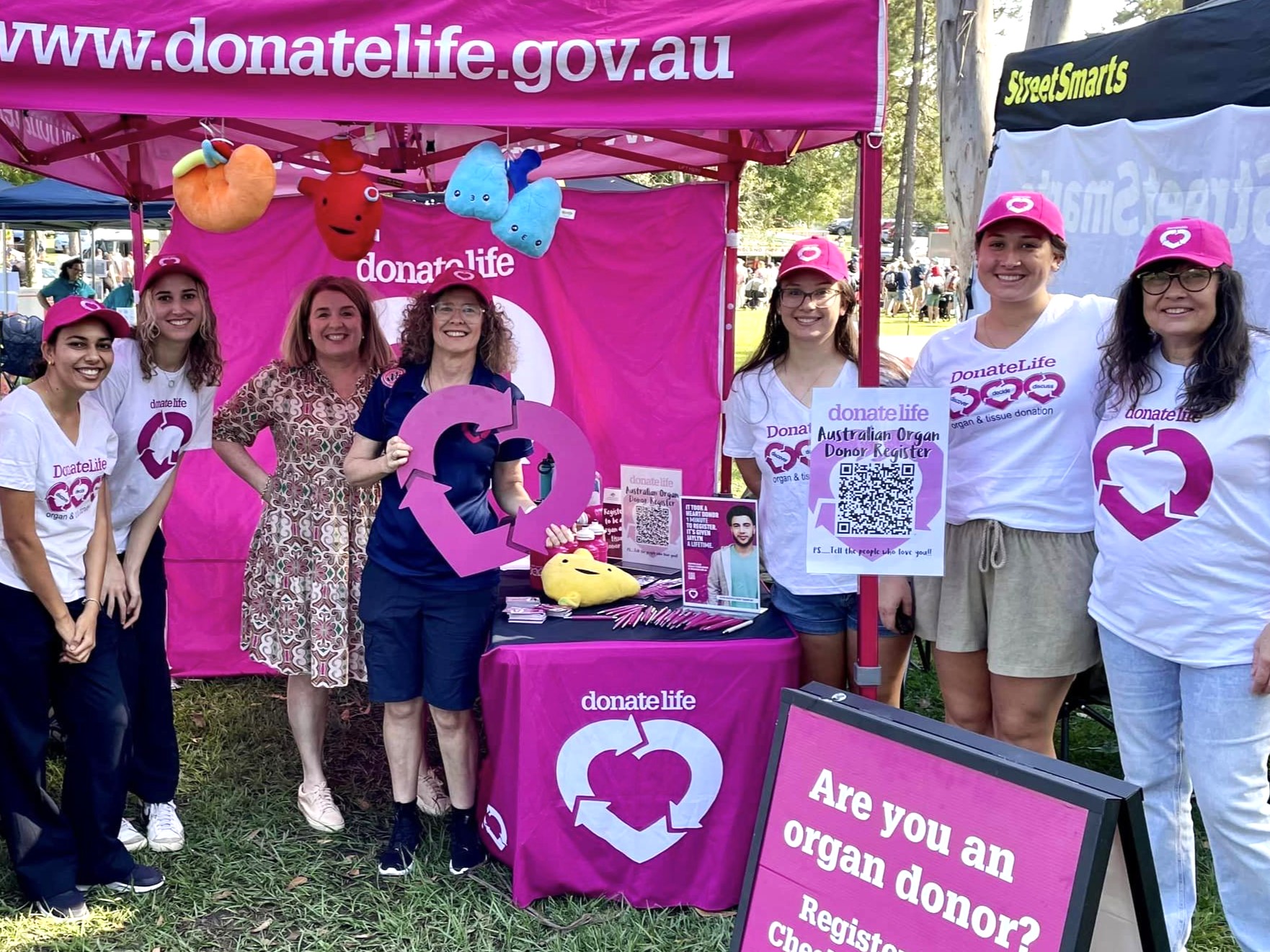 A group of women in DonateLife gear pose for a photo at a DonateLife stand during an expo. 