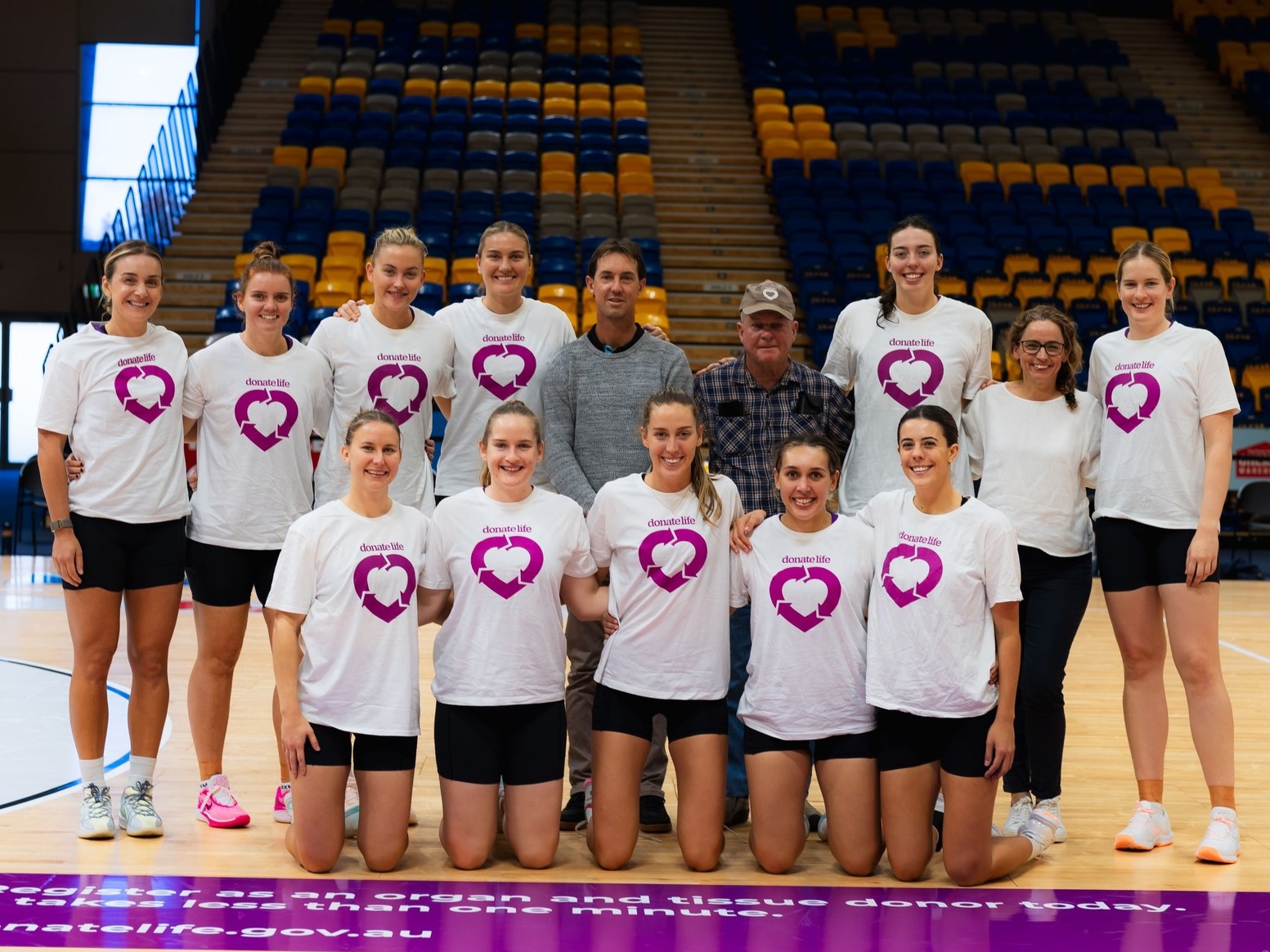 A team of netball players pose for a photo with two men.