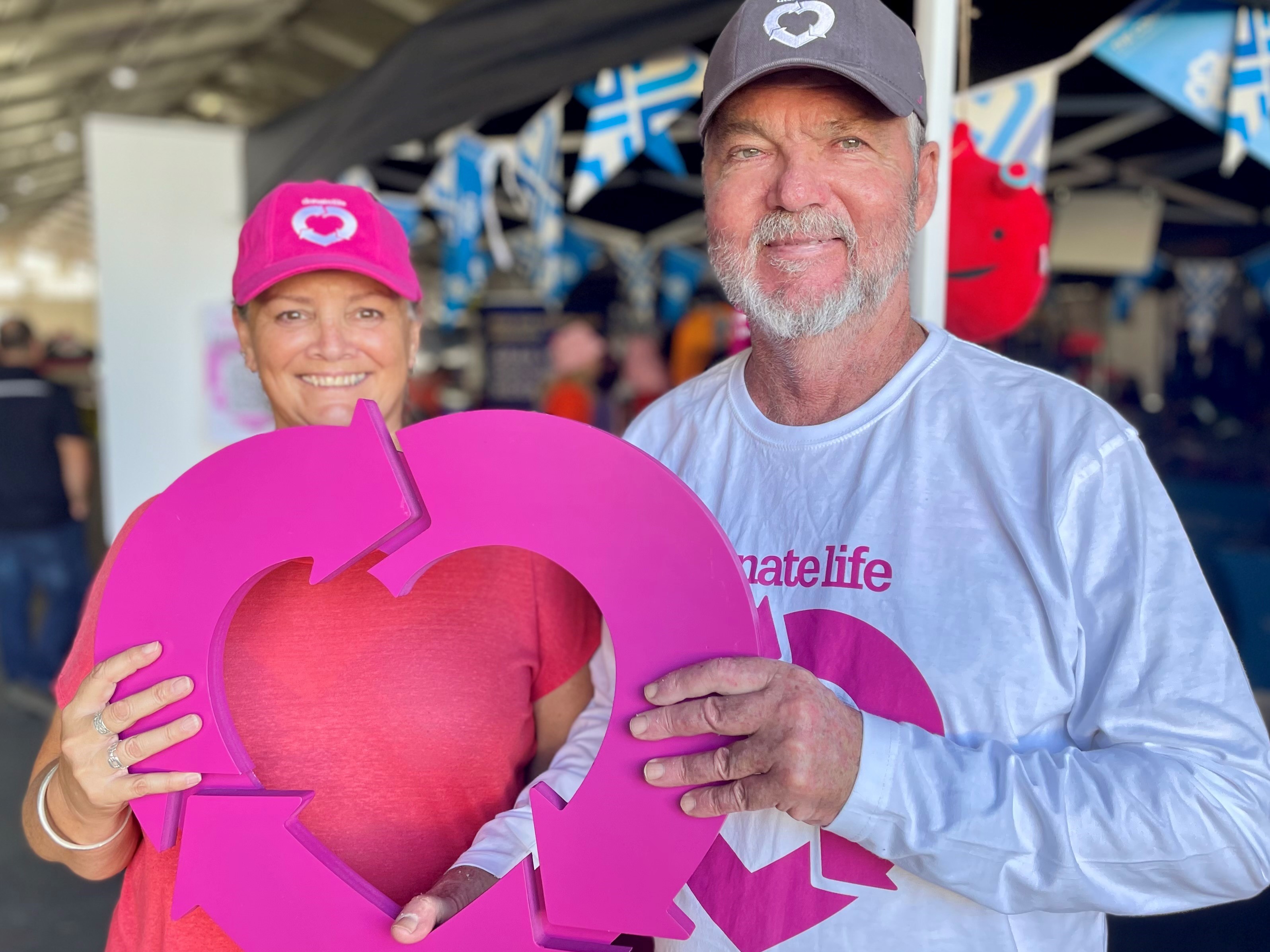 A woman and man hold up a wooden cut out of the DonateLife logo.