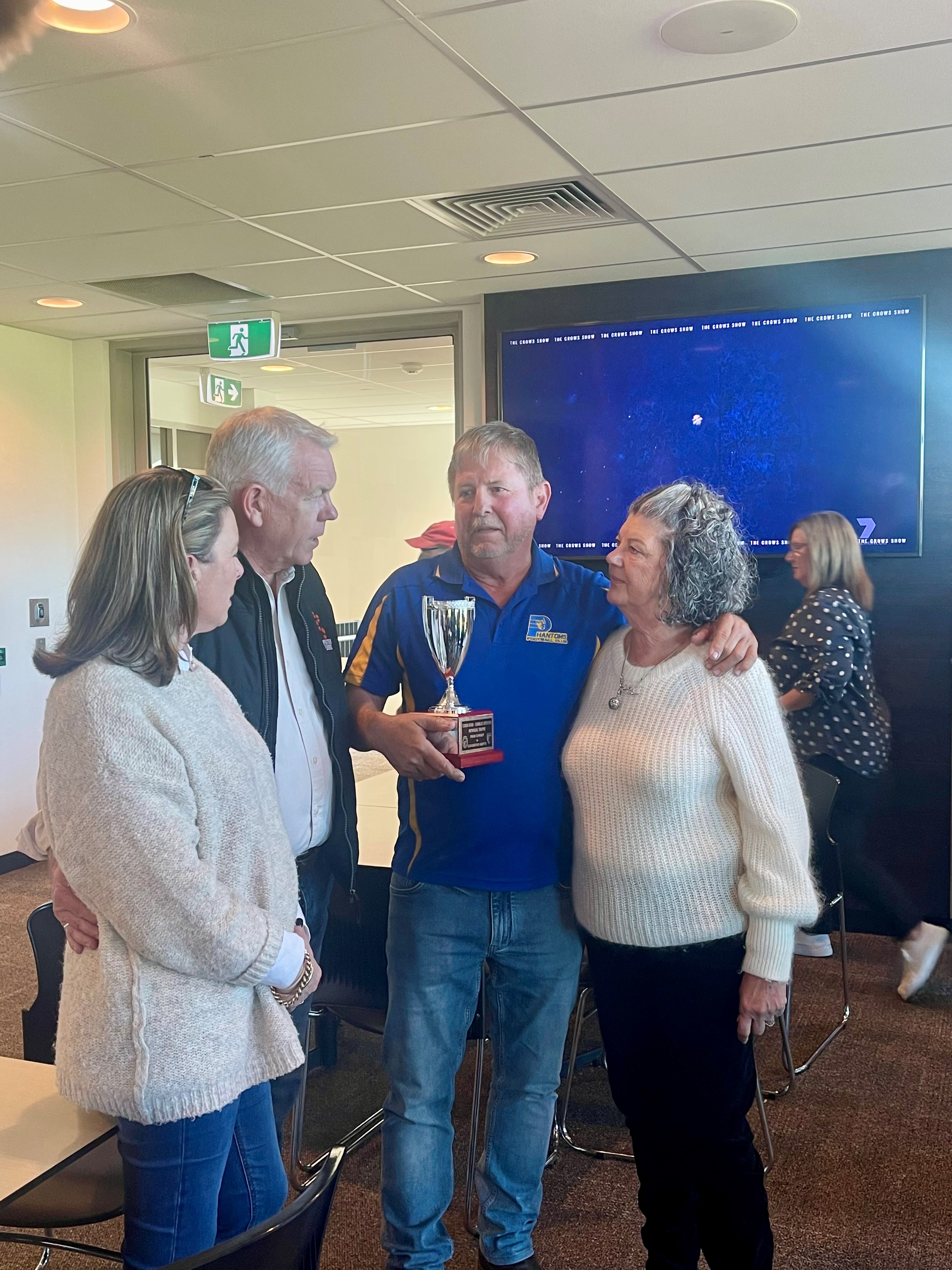 Four adults stand together chatting, one holding a silver trophy.