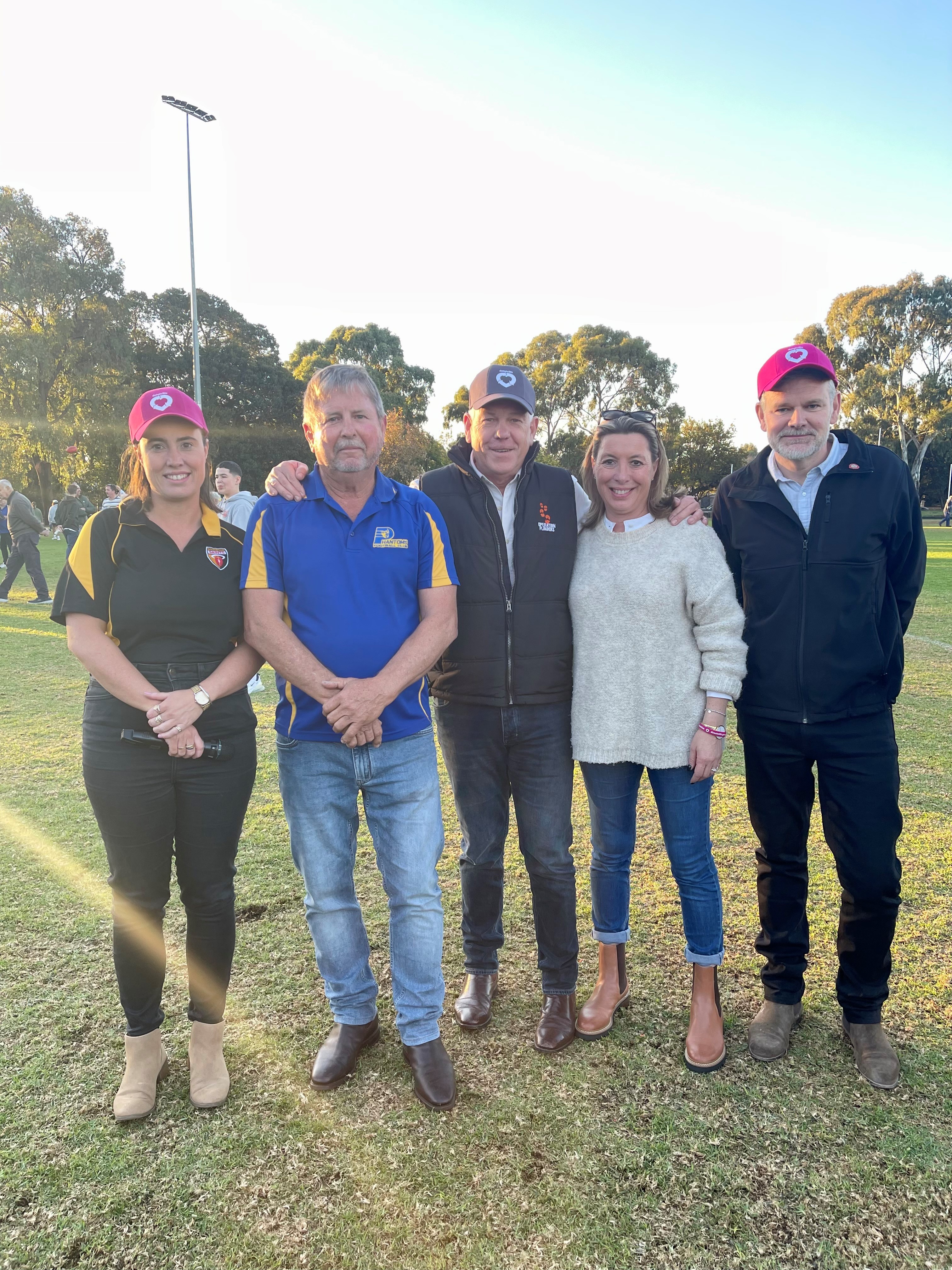 A group of five adults on a football oval pose for a photo.