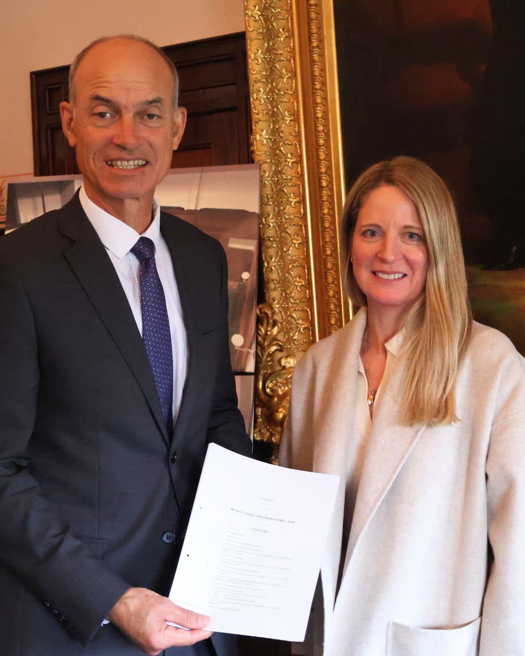 A man and a woman pose for a photo, holding up a piece of paper that has the amendment bill on it.