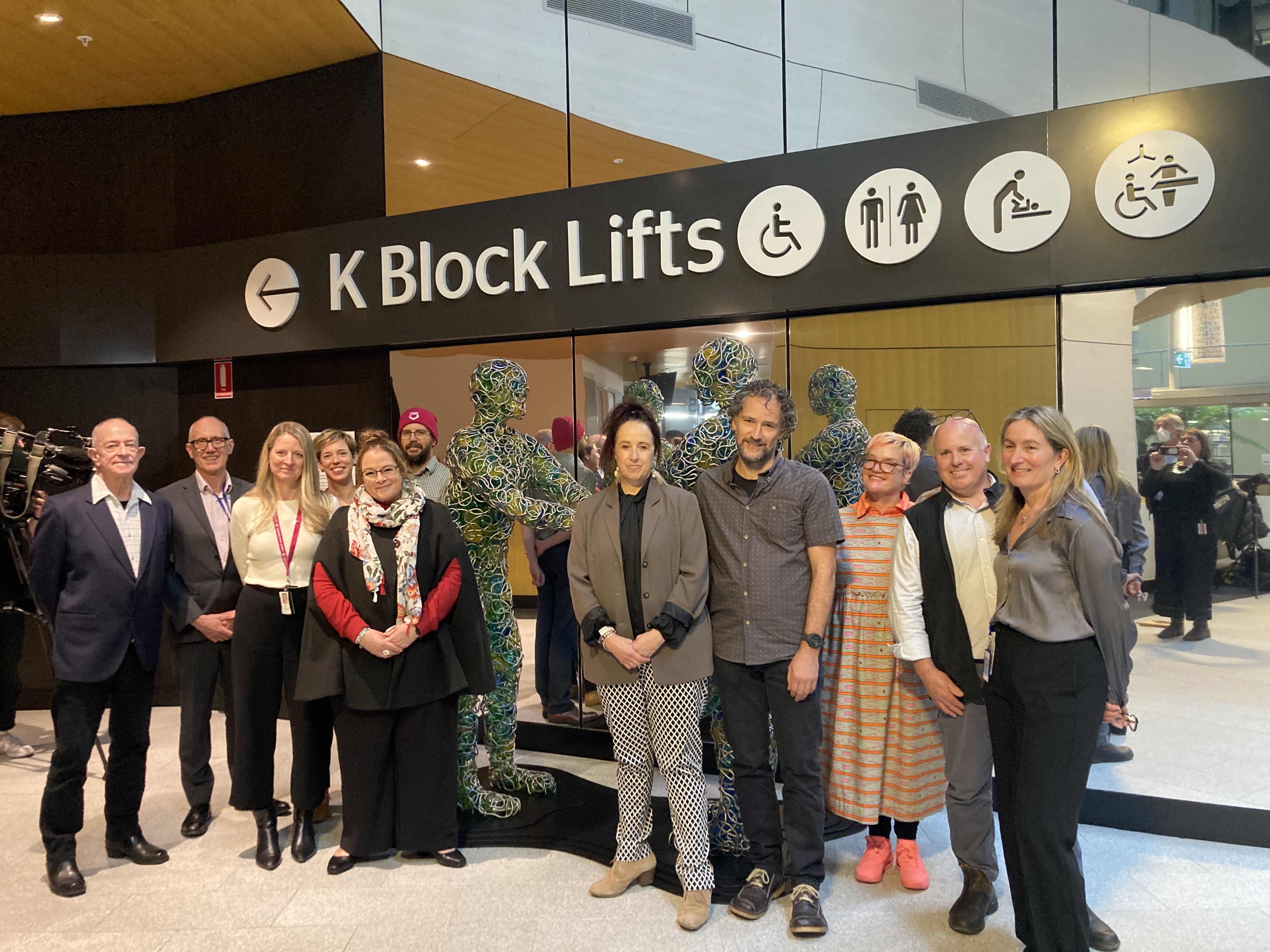 A group of people posing for a photo in front of a glass and metal sculpture.