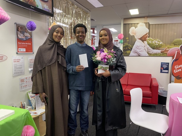 Two women and a man pose for a photo. One is holding a bunch of flowers.