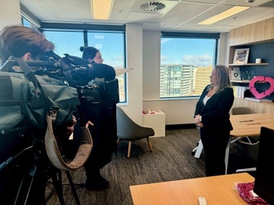 A video camera and journalist interviewing Lucinda Barry AM, OTA CEO standing in her corporate office. 