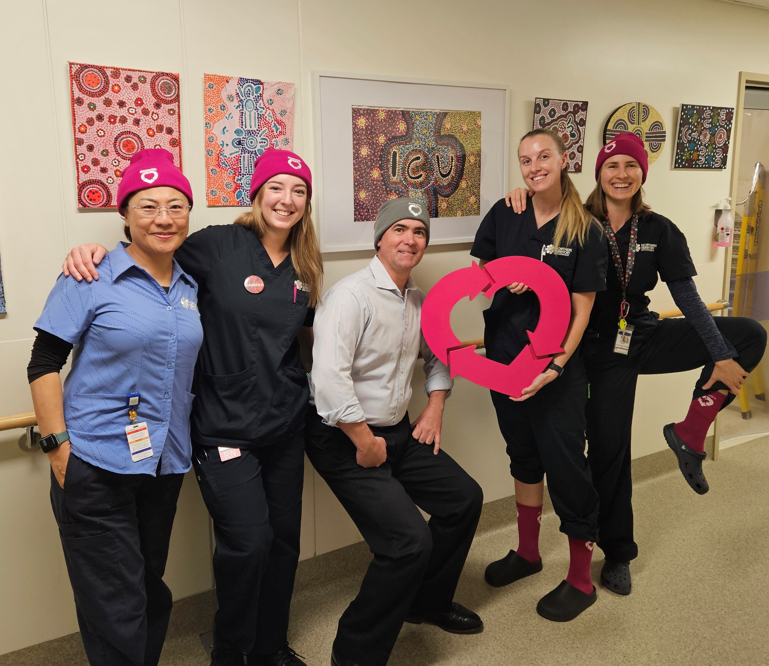 Five nurses pose for a photo together, wearing magenta DonateLife beanies and socks, and holding a DonateLife heart emblem.