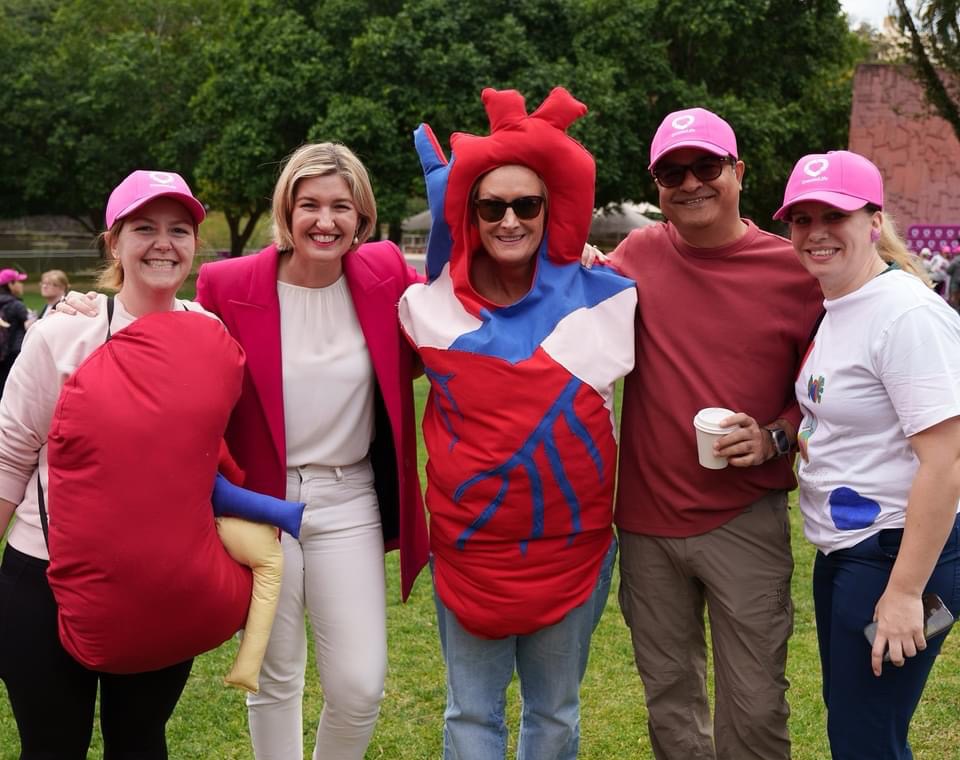 Five people pose for a photo; 2 of them are dressed up as organs. One is wearing an anatomical heart costume, and one is wearing a kidney costume.