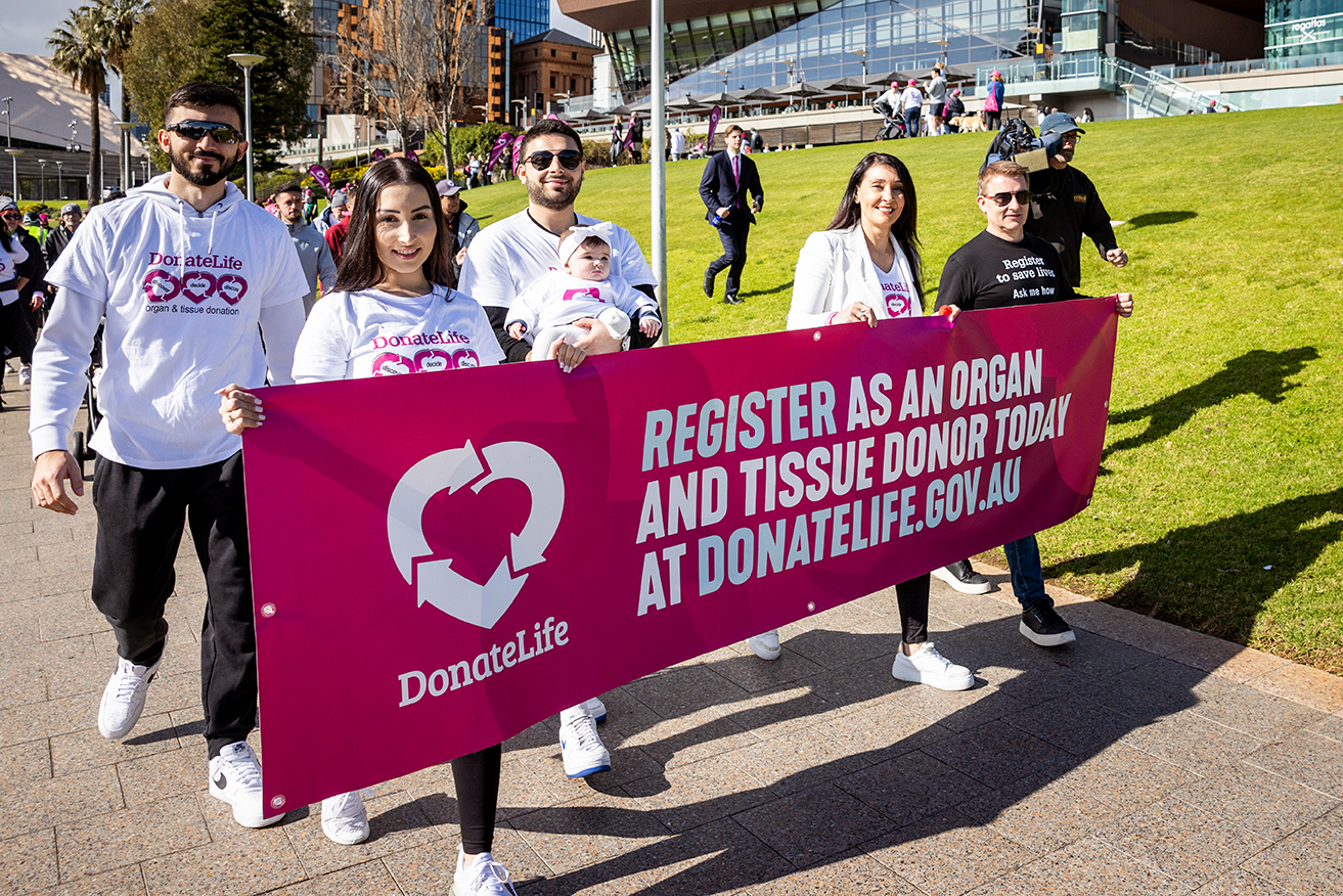 People holding a magenta DonateLife banner smile for the camera as they walk for the Step Up to Save Lives launch.