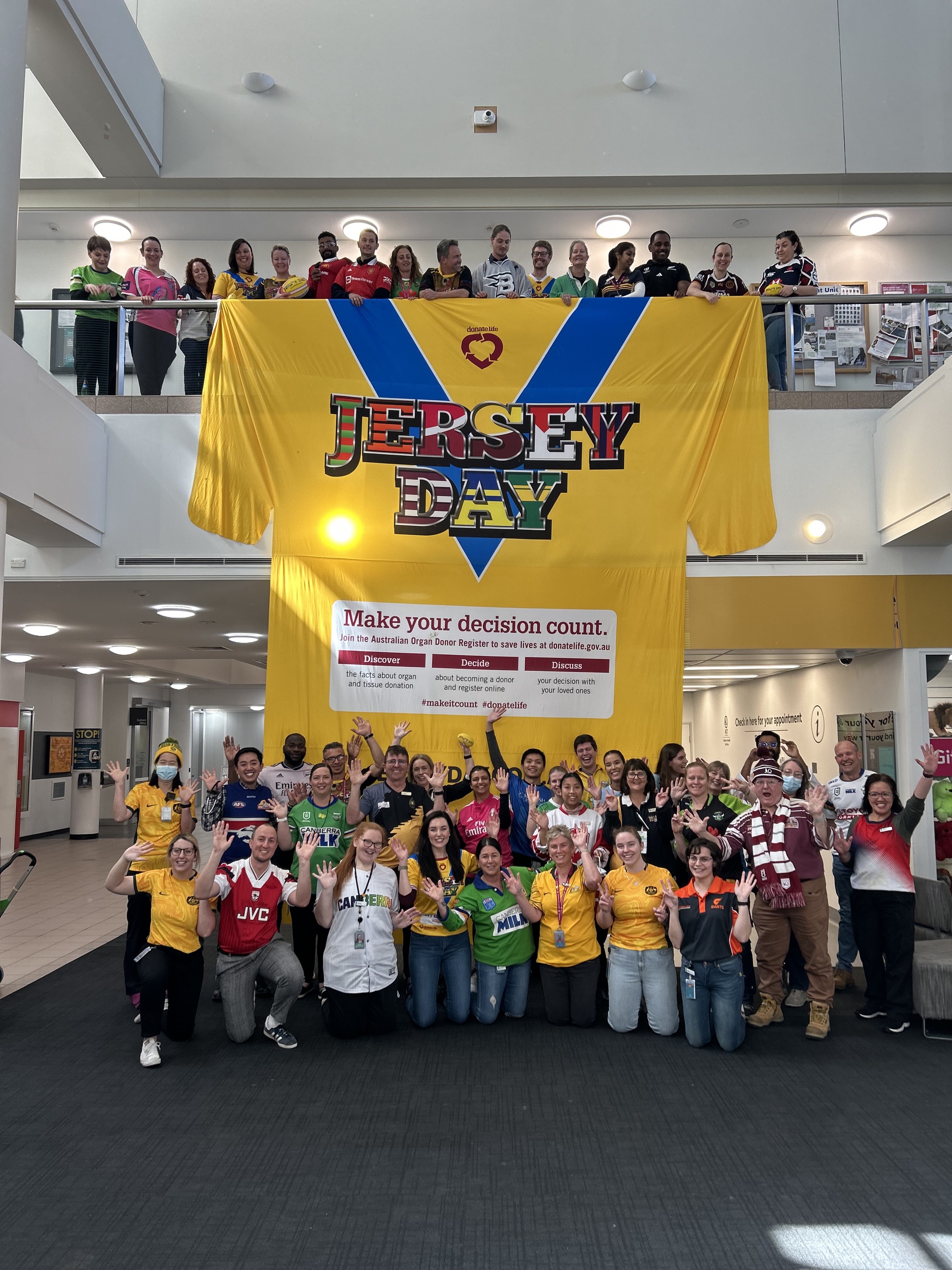 Staff at The Canberra Hospital pose in front of a giant Jersey Day banner in their favourite jerseys. 