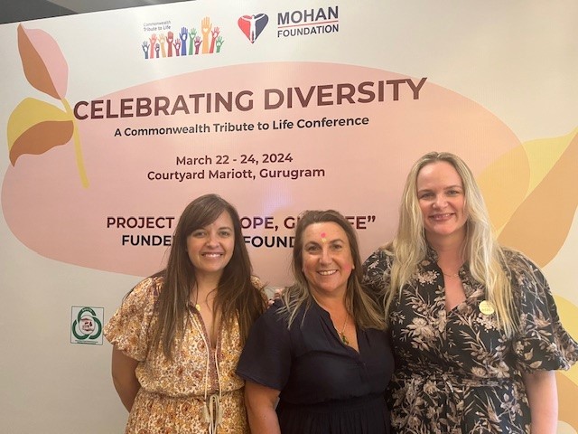 Three women posing for a photo in front of a conference sign.