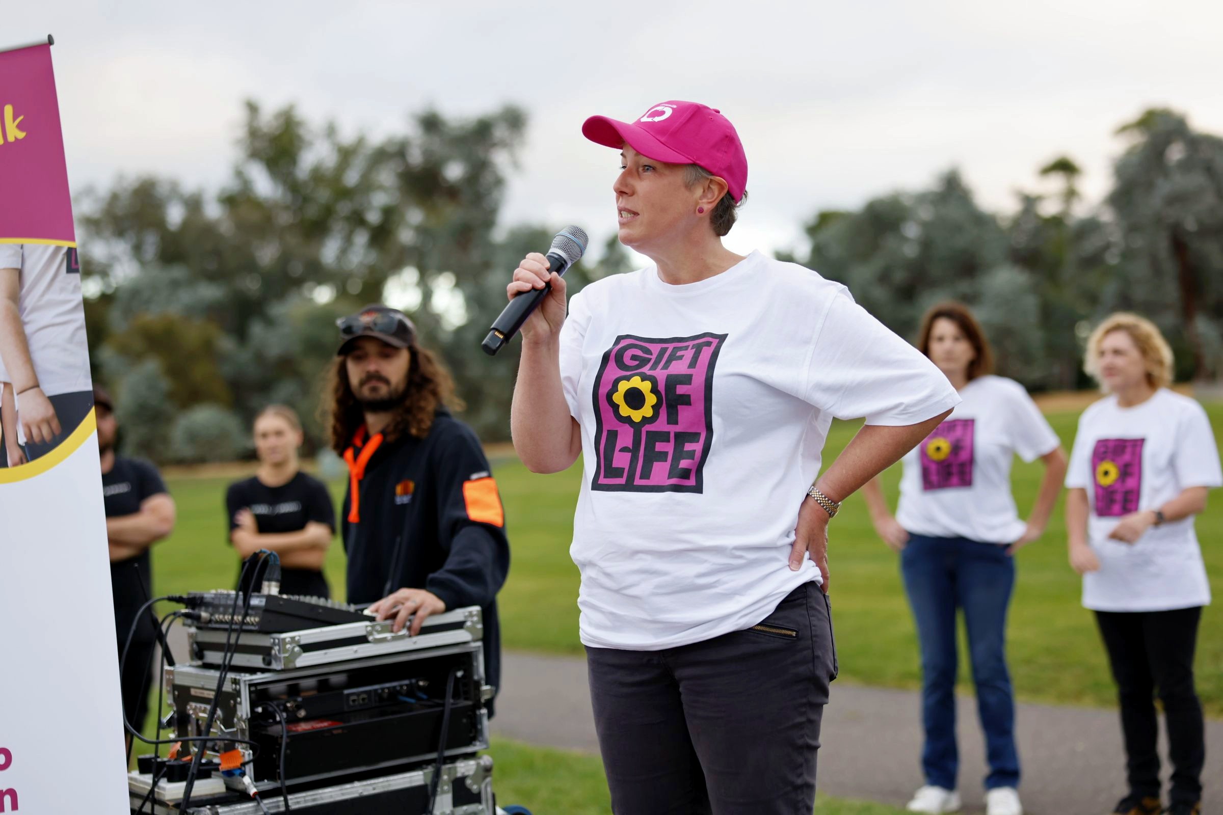 A woman dressed in a Gift of Life shirt and a DonateLife cap talks into a microphone. 