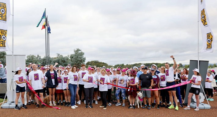 A group shot of Gift of Life Walk attendees, dressed in Gift of Life shirts, beginning the walk by walking through a start ribbon.