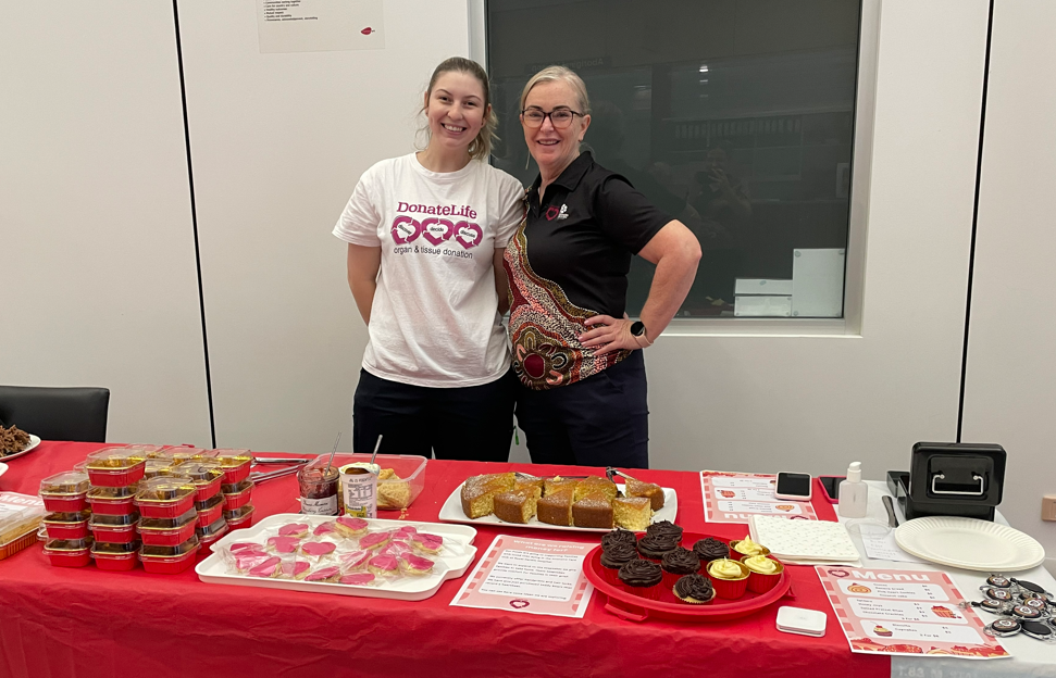 Two DonateLife staff at the bake sale stand, a table of baked goods in front of them. 