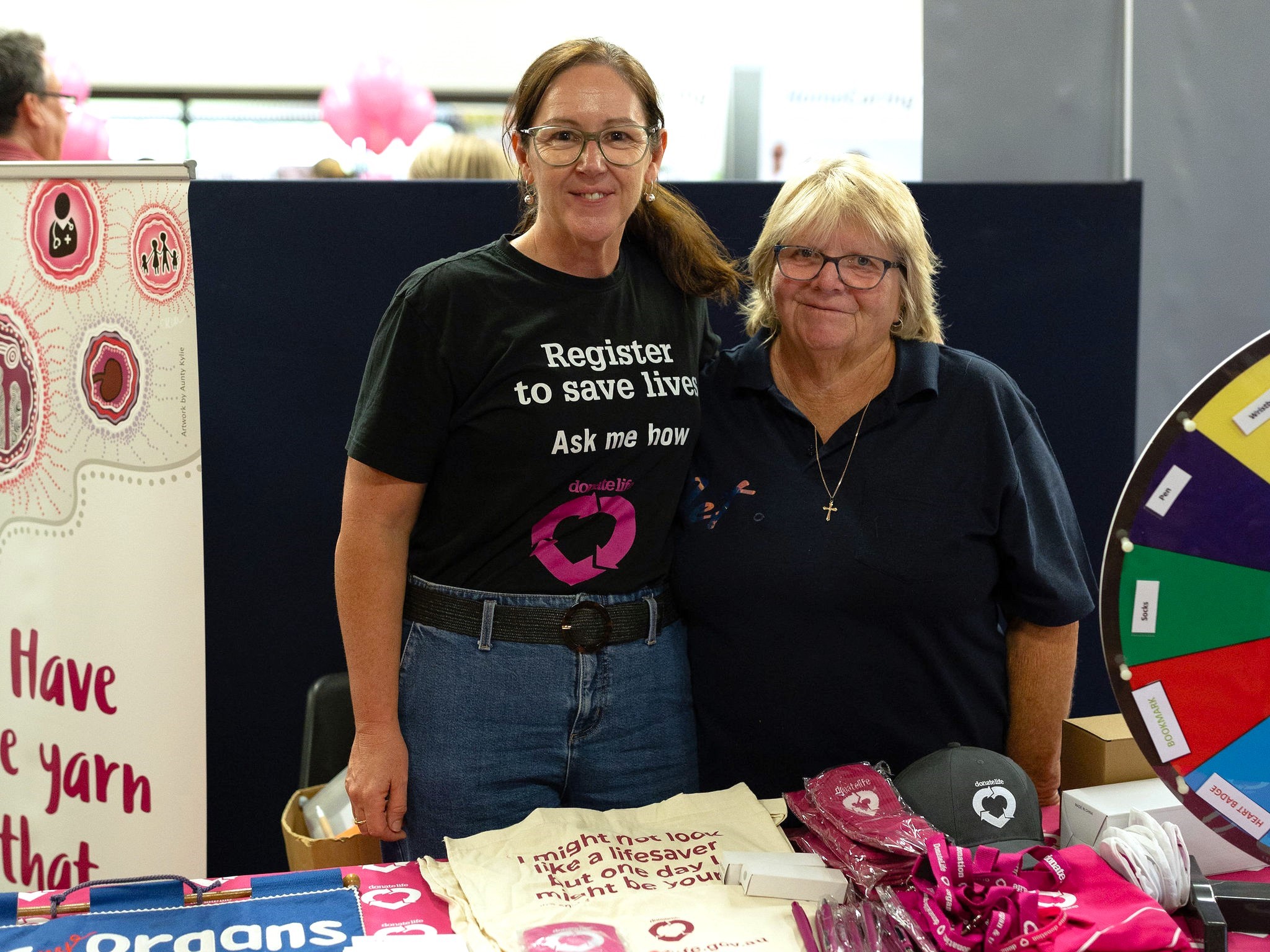 Two women stand together behind a DonateLife expo table, smiling at the camera.