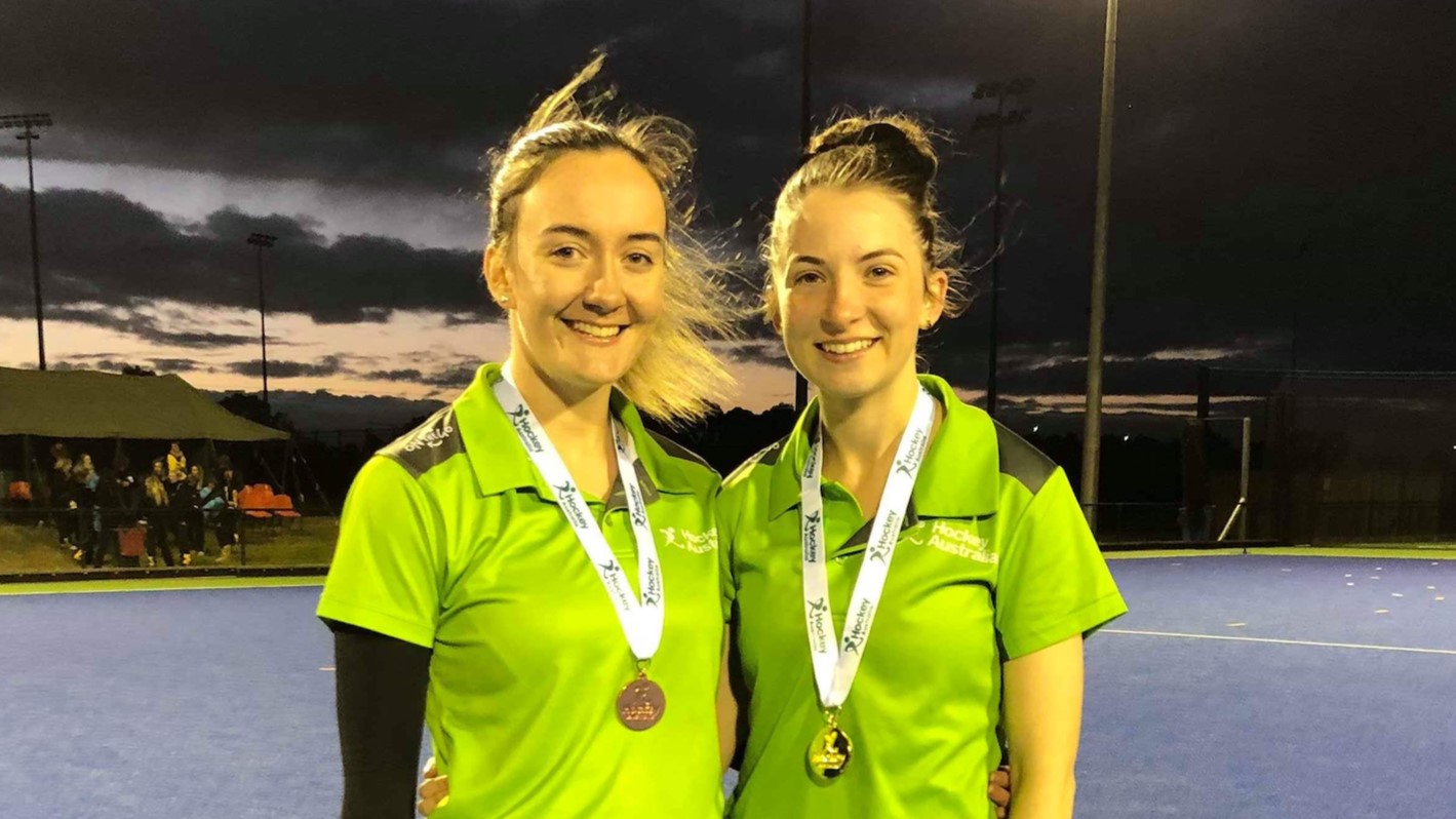 Two people standing together for a photo, wearing hockey umpire shirts and wearing medals around their necks.