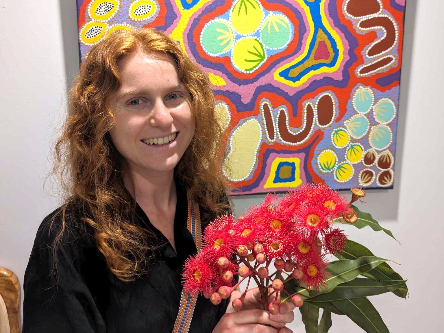 A photo of a woman with long red hair, holding a bunch of red wattle flowers.