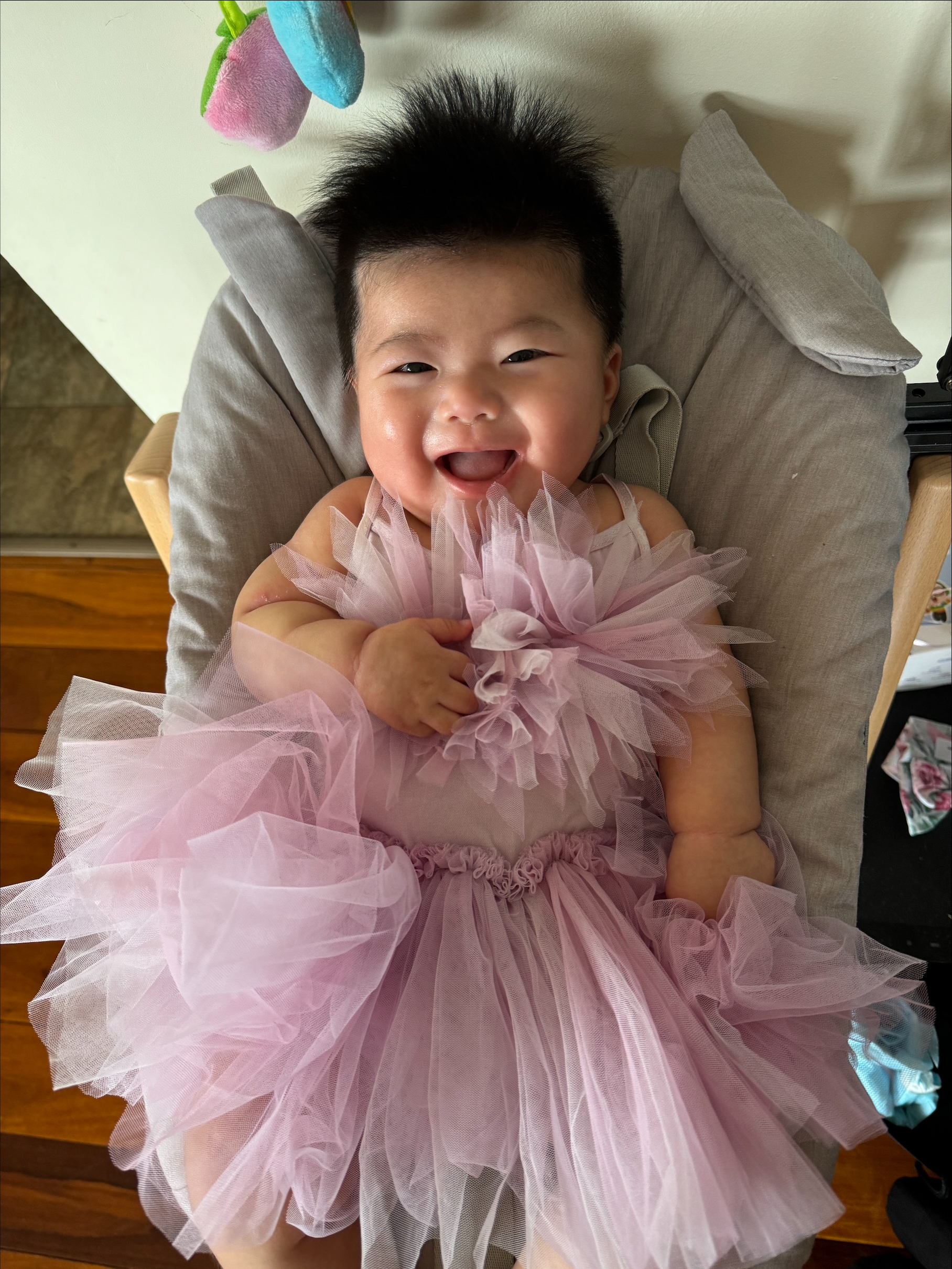 A photo of a baby wearing a pink tutu dress and laughing at the camera. 