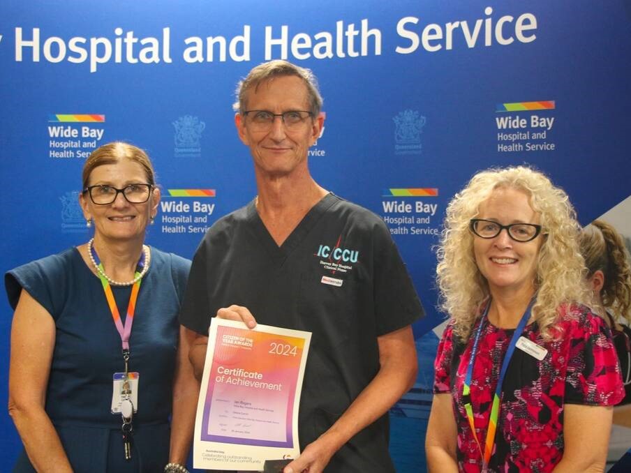 Three people smiling for the camera. The man in the middle is holding up an award certificate.