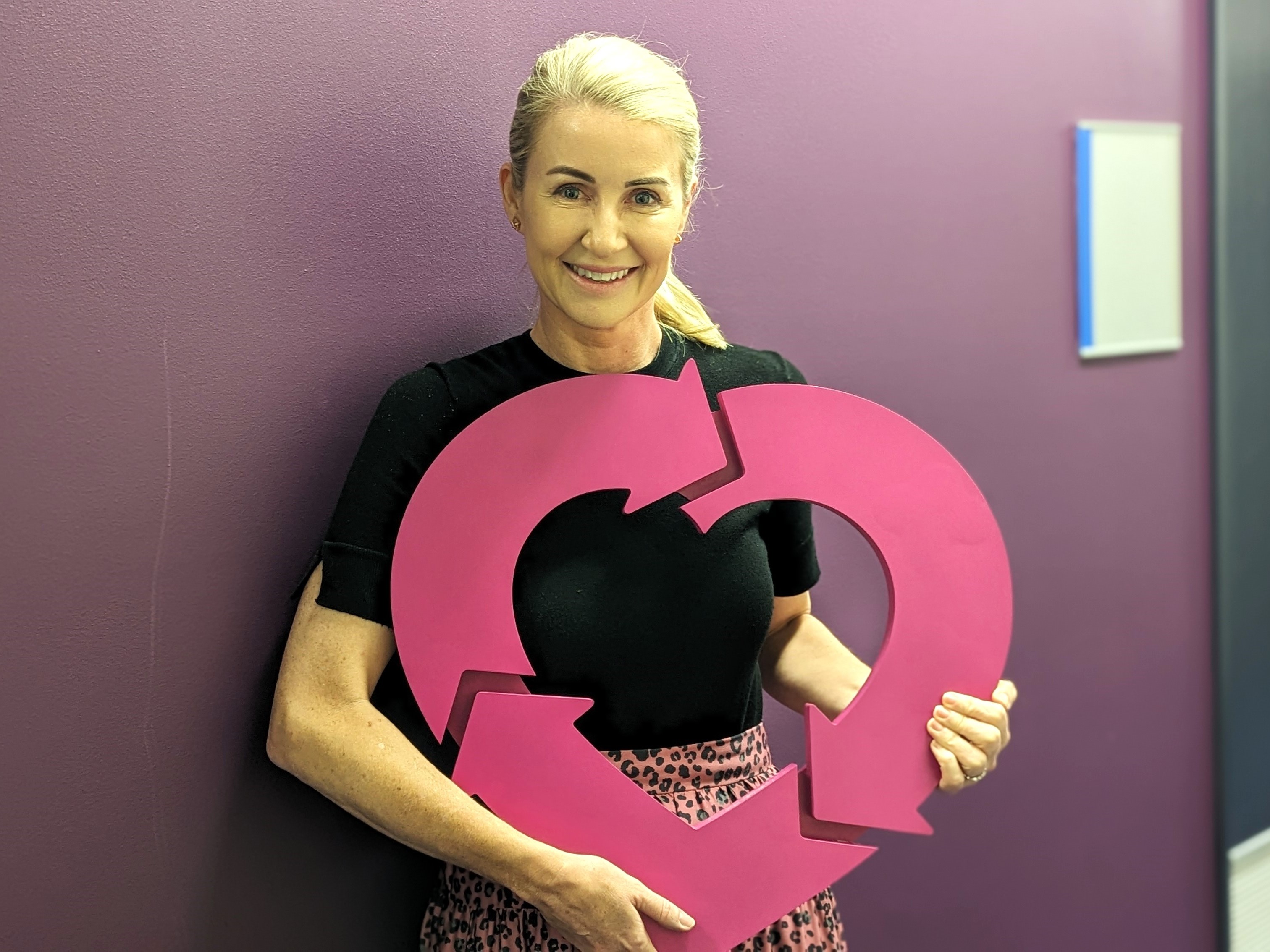 A photo of a woman holding a DonateLife heart emblem, smiling at the camera