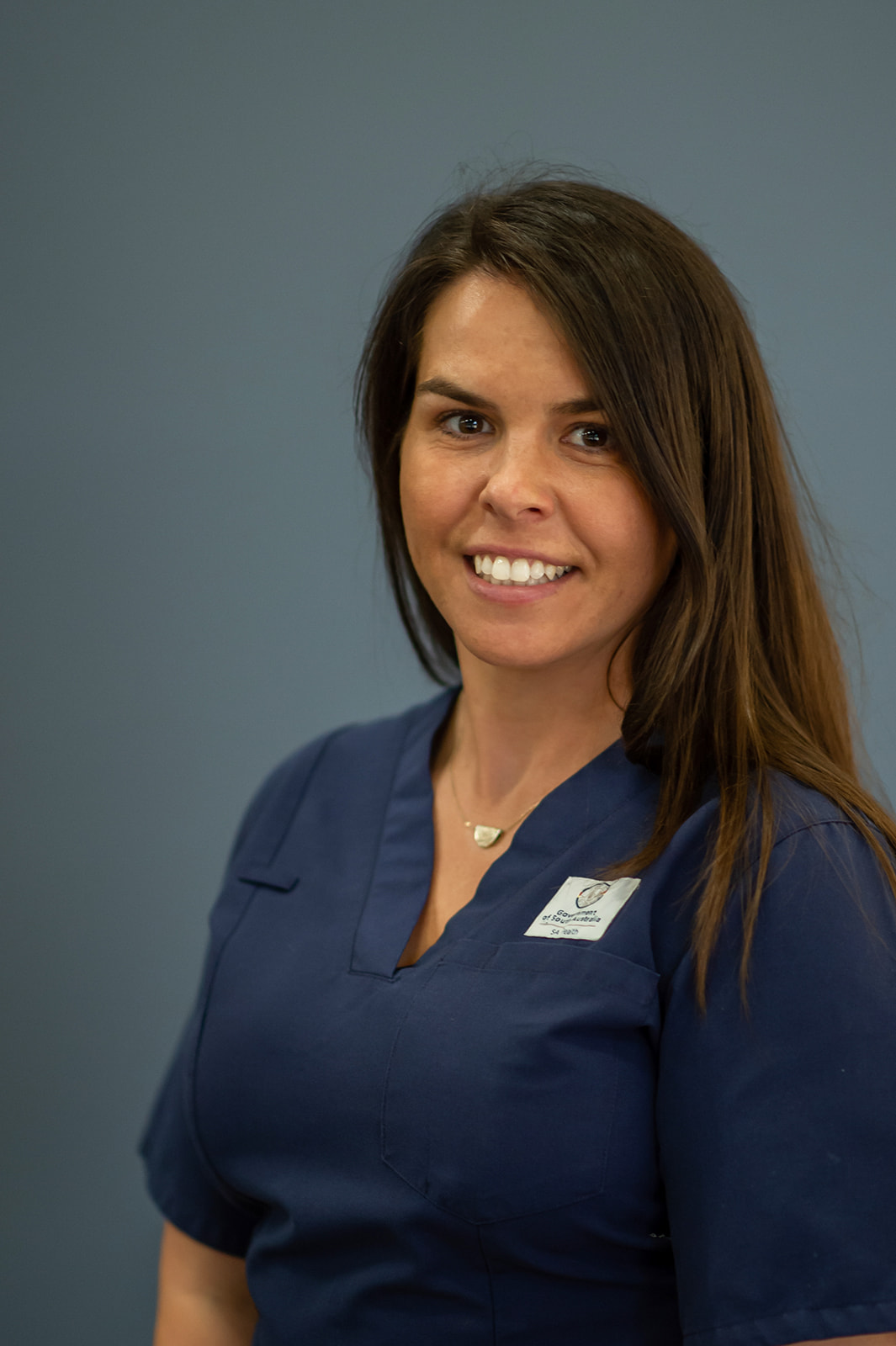 A woman wearing dark blue scrubs smiling at the camera.