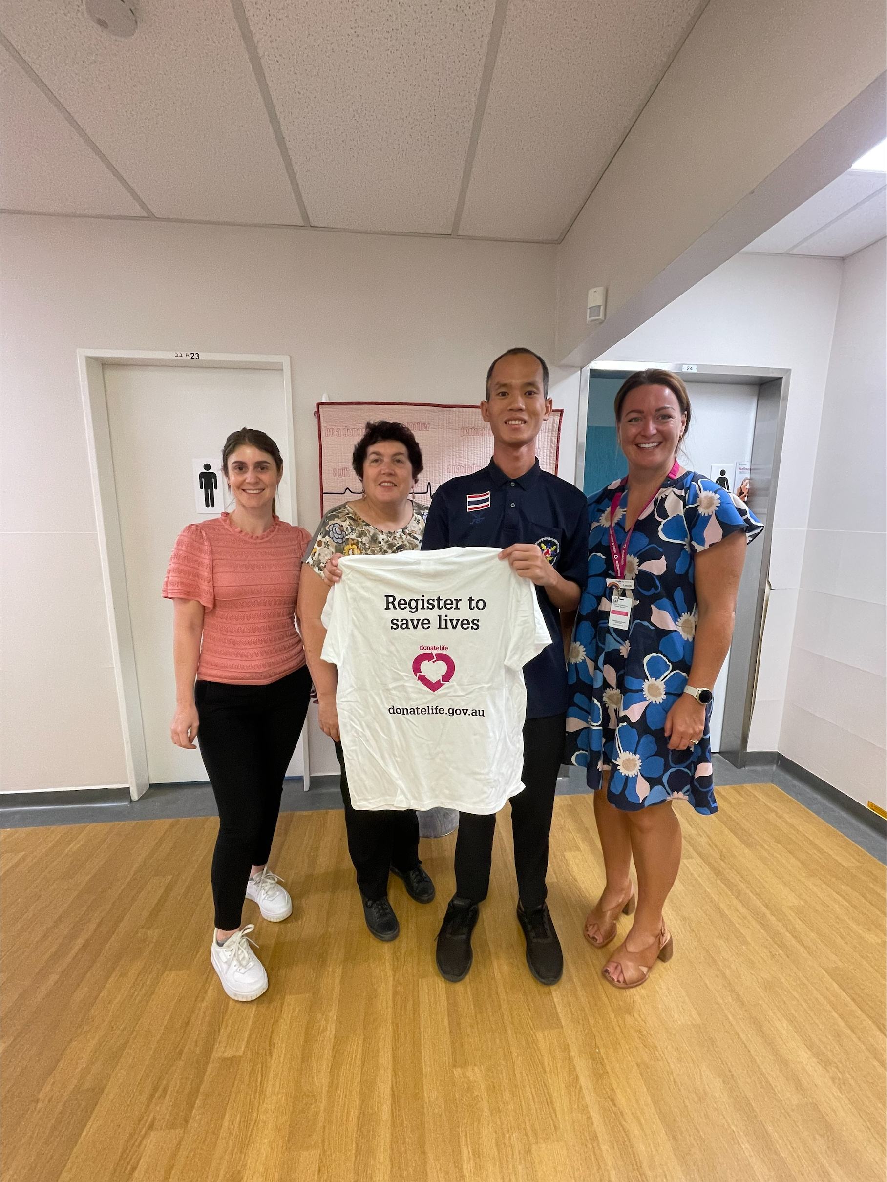 Four people stand together for a photo, holding up a ‘register to save lives’ DonateLife tshirt.