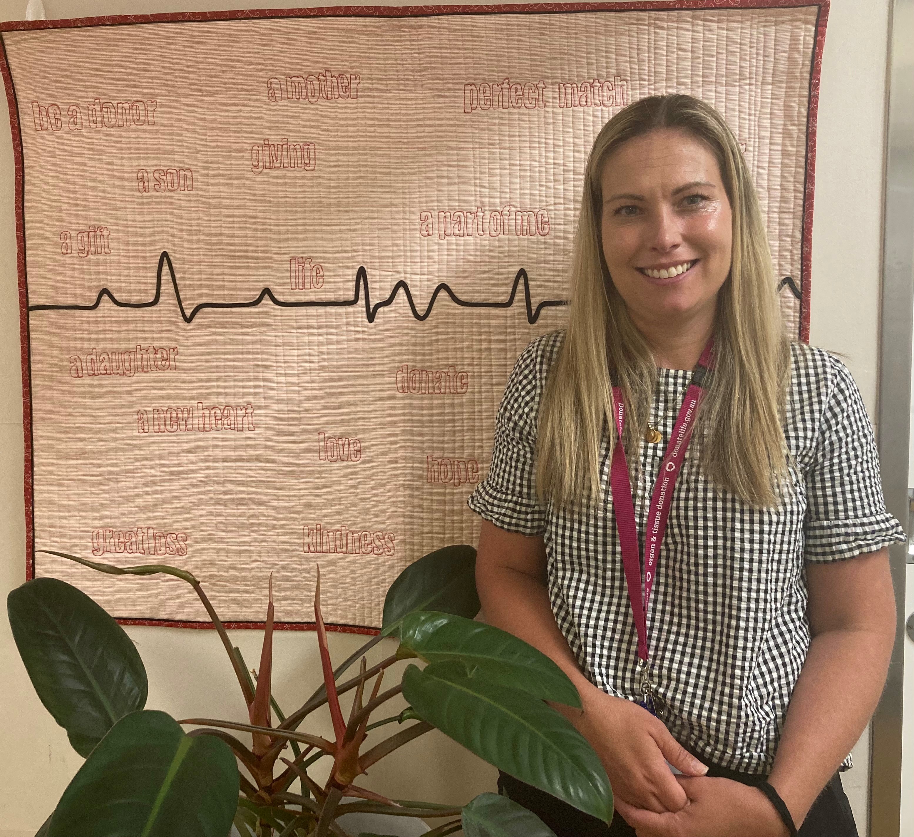 A woman, standing in front of an artwork of a heartbeat pulse line, smiles at the camera.