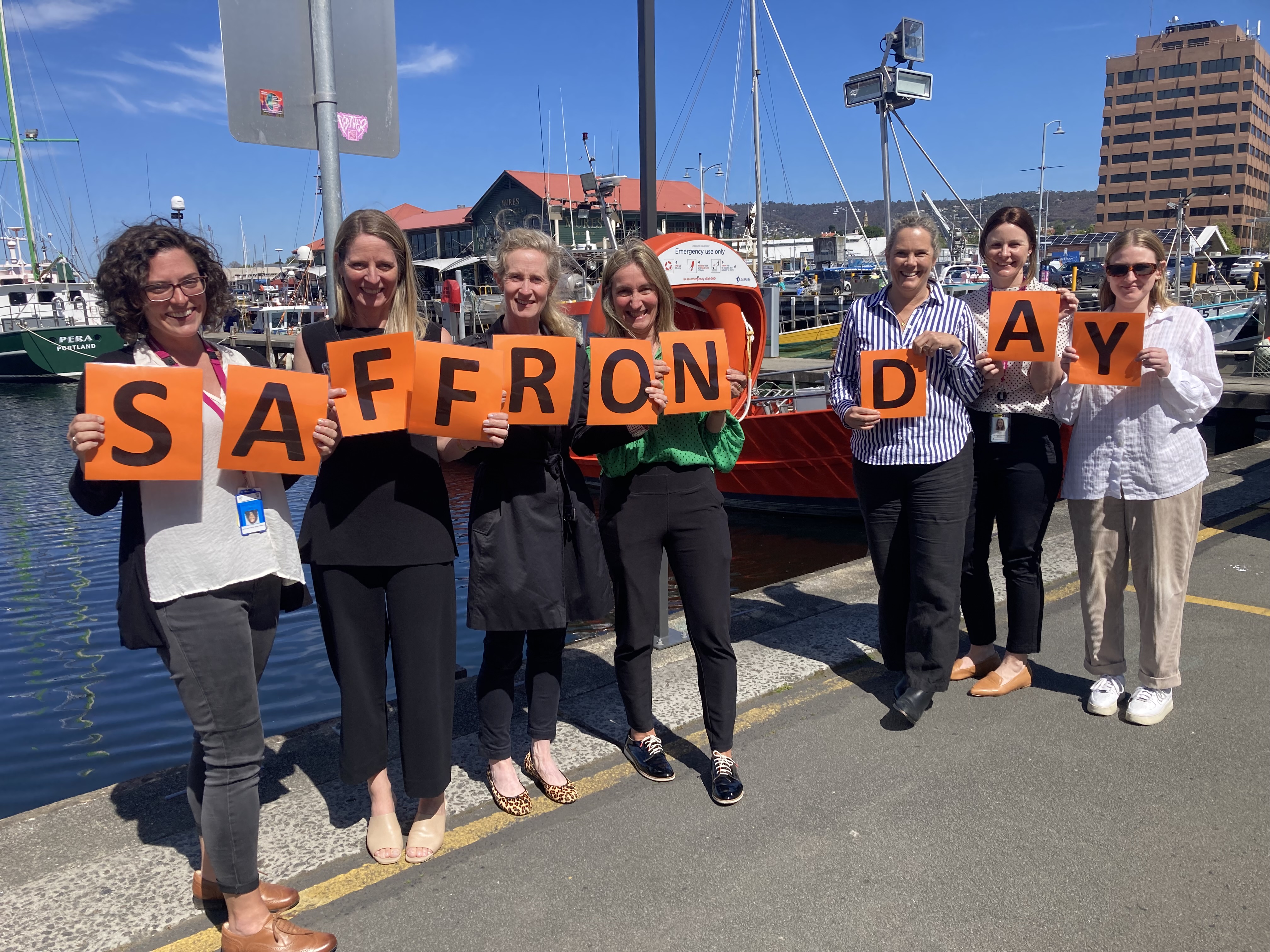 The DonateLife Tasmania team hold up orange letters spelling out ‘Saffron Day’ at the Hobart waterfront.