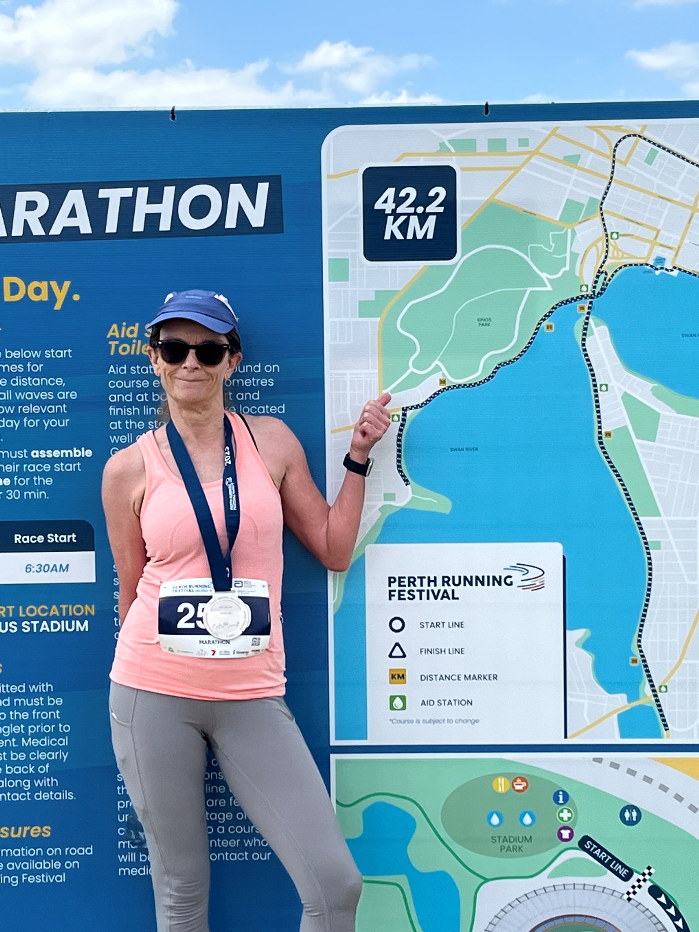 Julie Crouch poses with her Perth Marathon medal in front of a map of the marathon route.