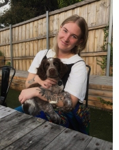 A woman sitting at an outside table, smiling at the camera, with a Springer Spaniel puppy in her arms.